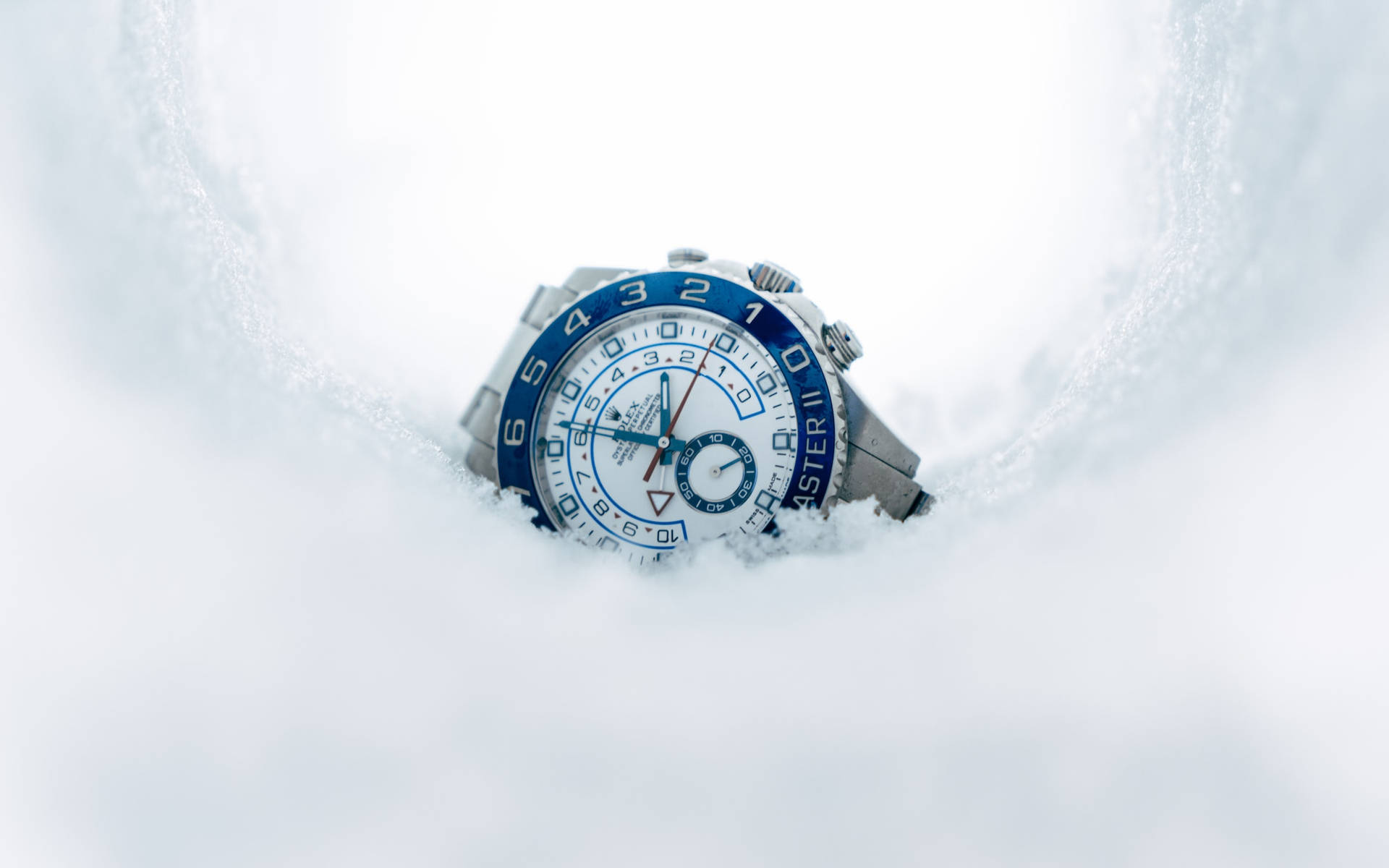 雪 桌布 壁紙 — 一隻藍銀色計時碼錶從雪堆中浮現，周圍是清晰的冬季紋理。