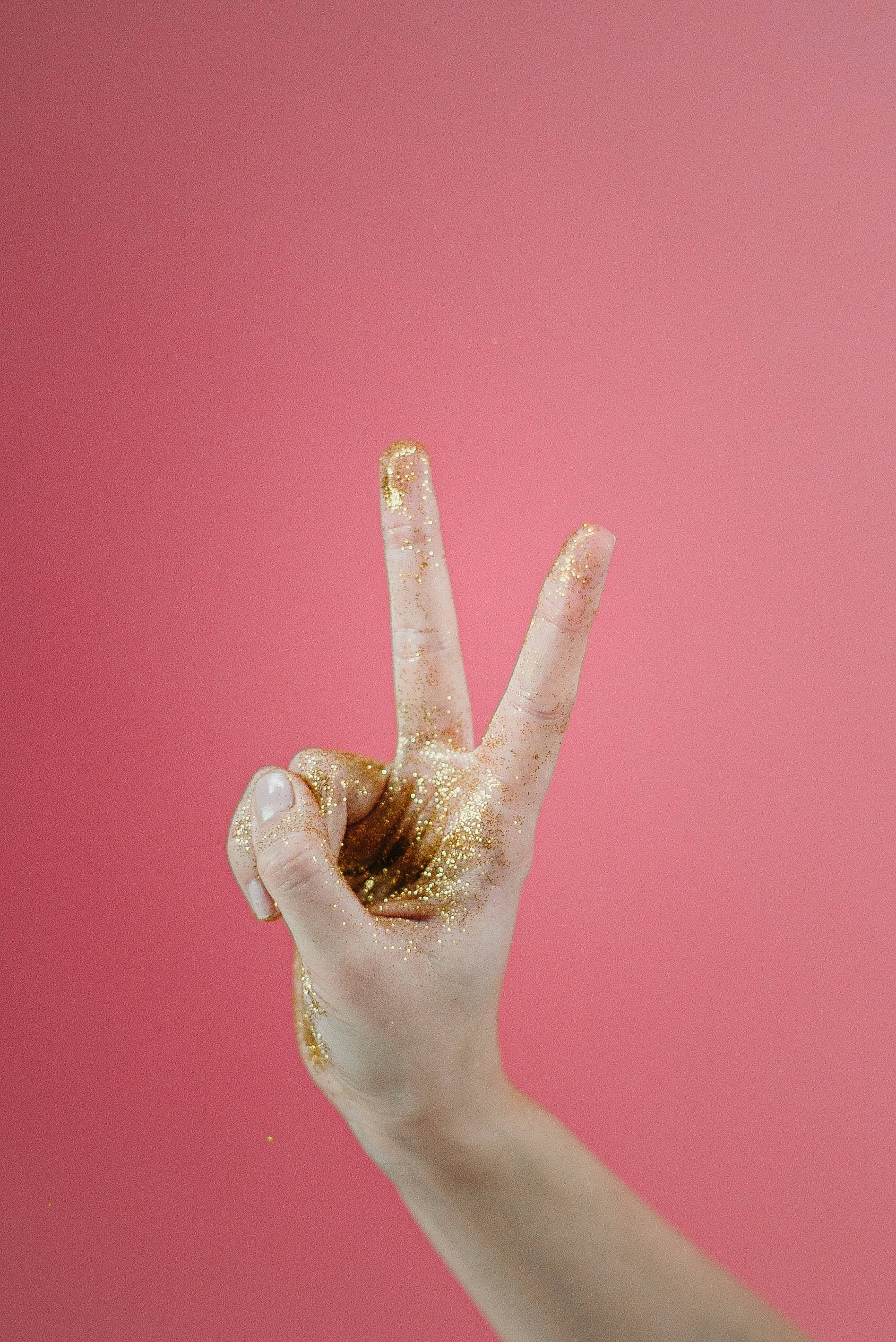 Peace Symbol 桌布 壁紙 — 一隻覆蓋著金色亮粉的手在純粉紅色背景上做出和平手勢。