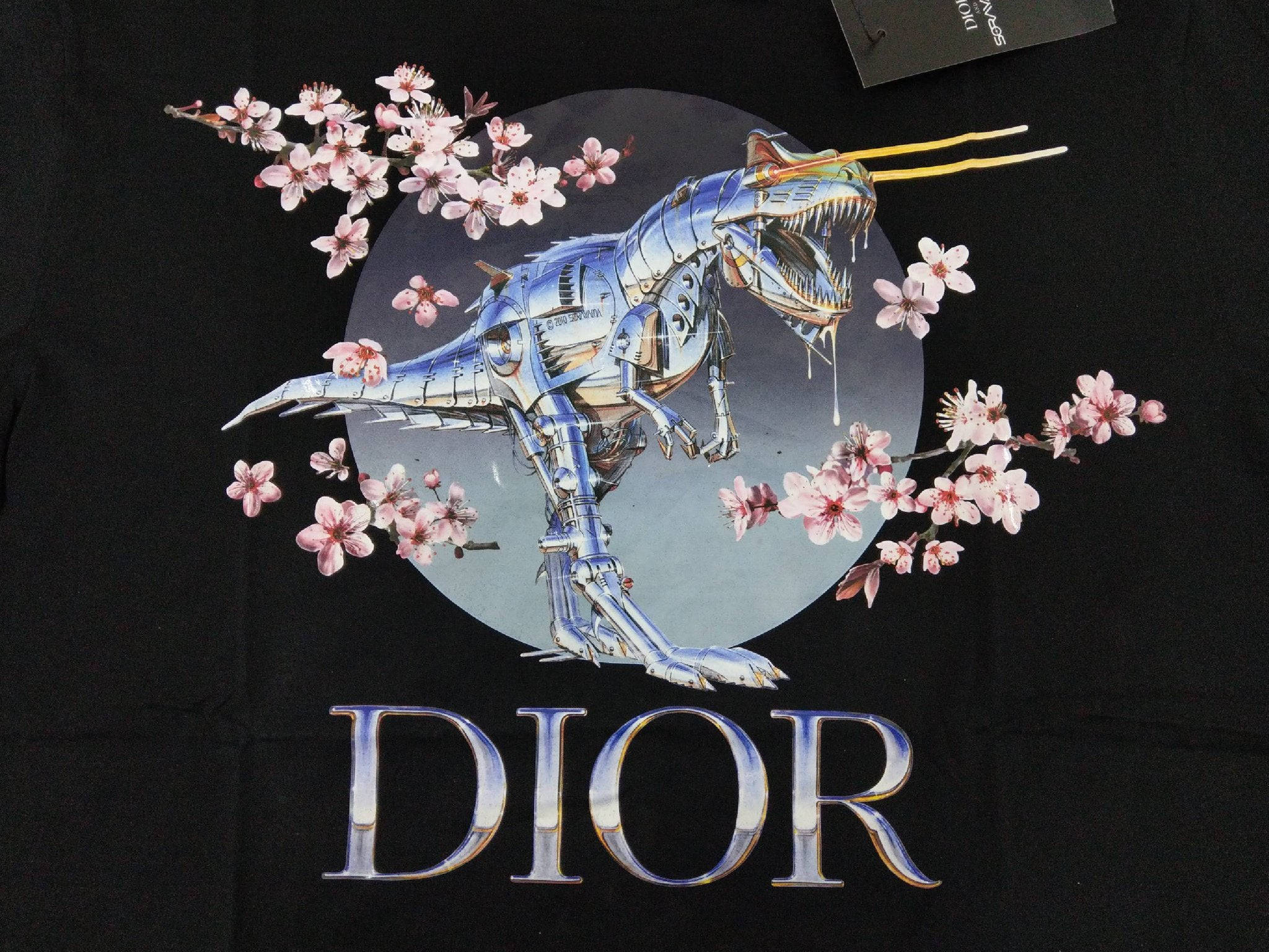 Dior 動態 桌布 壁紙 — 一隻金屬藍色機械恐龍，嘴裡叼著筷子，被粉紅色櫻花包圍，印在帶有DIOR標誌的黑色T恤上。