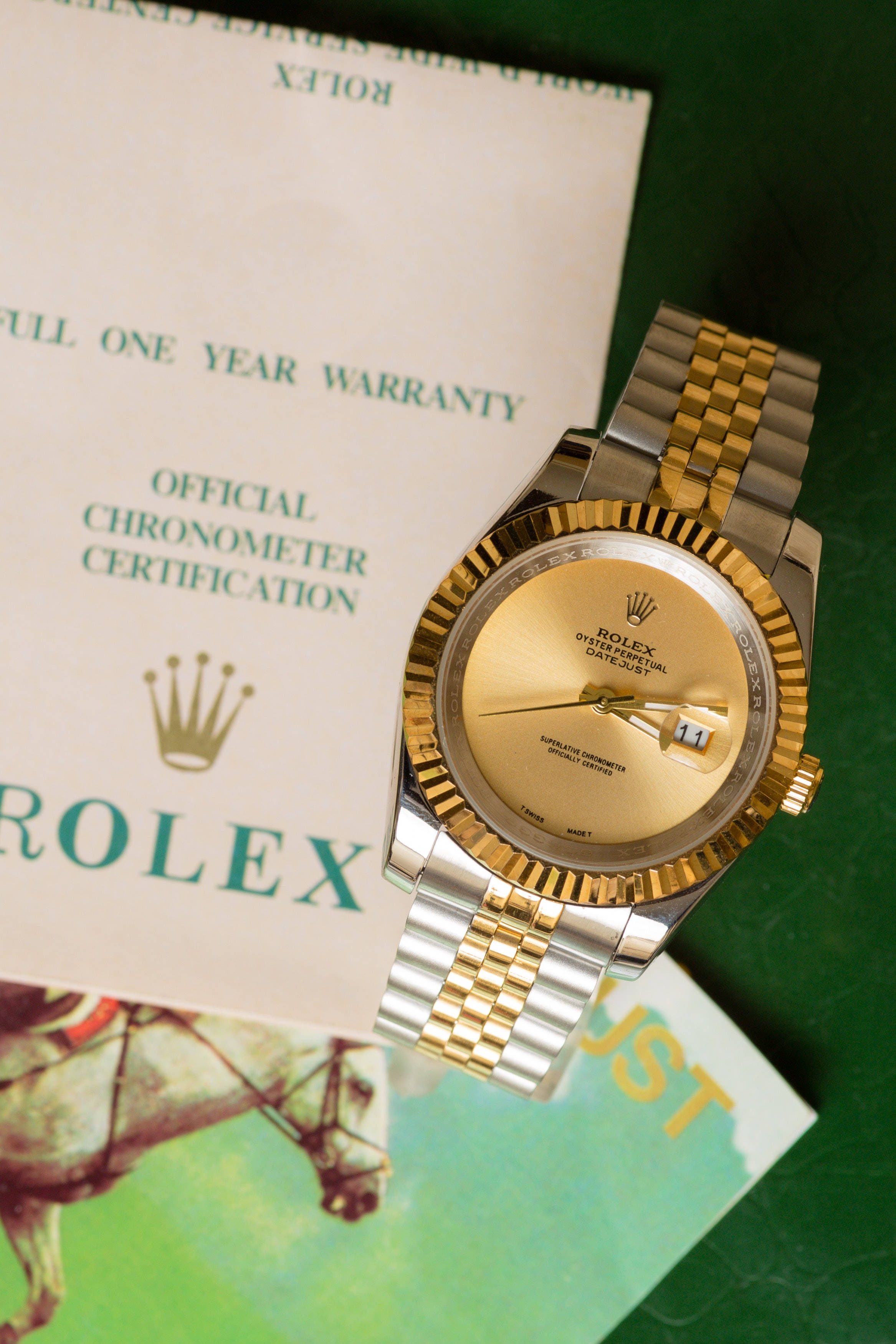 標誌 桌布 壁紙 — 一隻金色和鋼製的勞力士Oyster Perpetual Datejust手錶放在綠色表面上的官方保固證書和認證文件上。