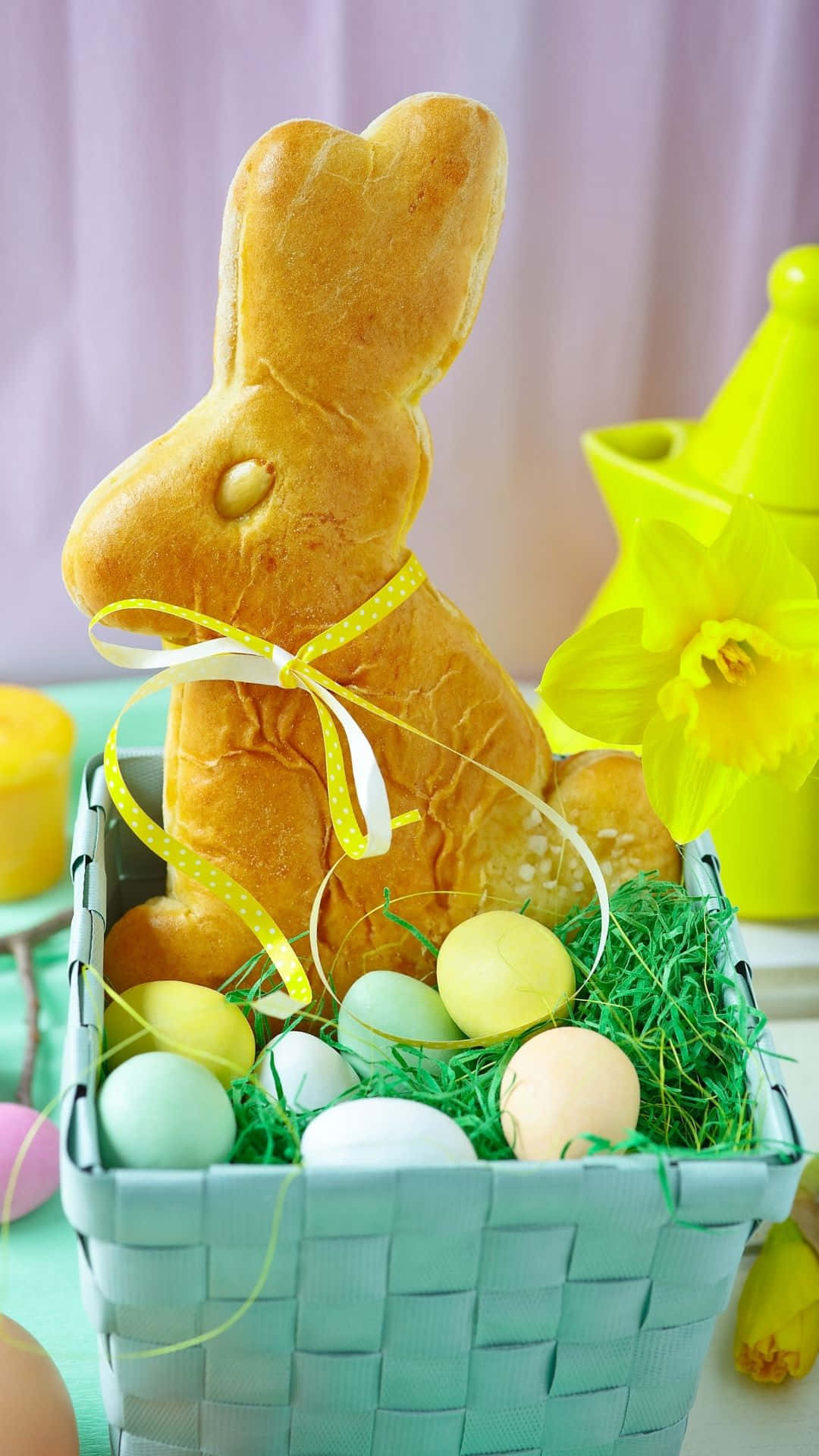 Easter Bunny 桌布 壁紙 — 一隻金色麵包兔坐在柳條籃裡，旁邊有粉彩蛋、青草和一朵黃色水仙花。