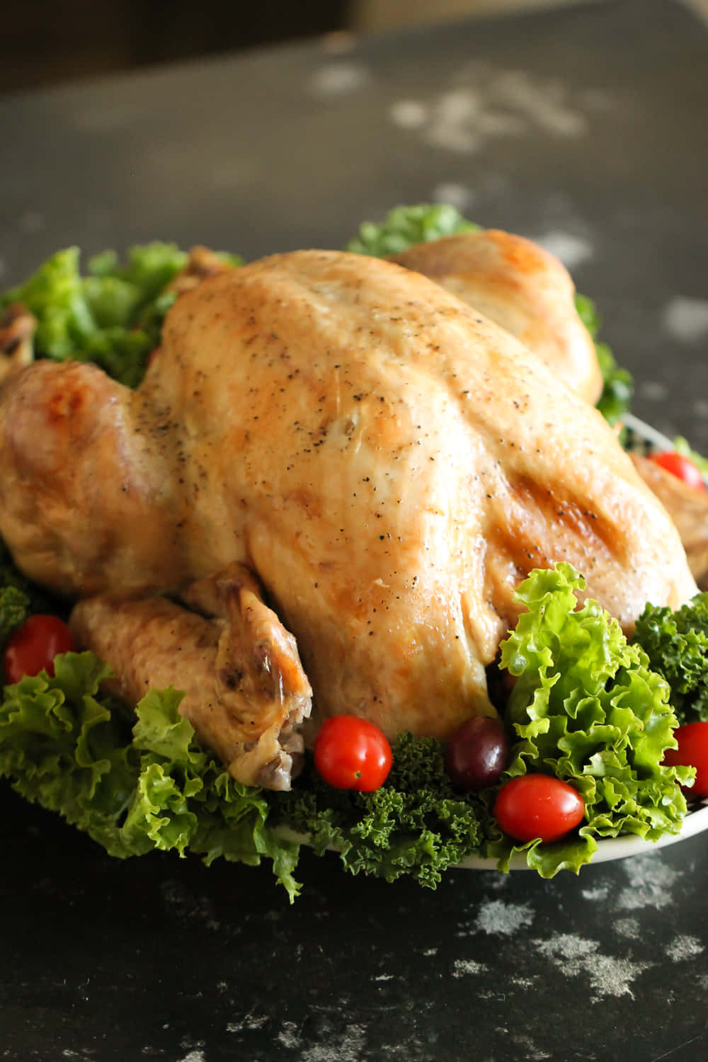 感恩節 桌布 壁紙 — 一隻金黃色的烤全雞，配上新鮮生菜和櫻桃番茄，放在深色斑點檯面上。