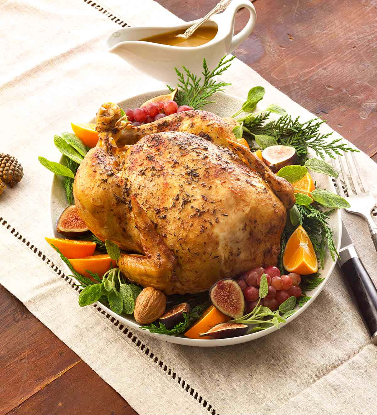 Turkey Happy Thanksgiving 桌布 壁紙 — 一隻金黃色的烤火雞，周圍擺滿無花果、柳橙、葡萄和香草，放在白色托盤上，置於鄉村風木桌上。