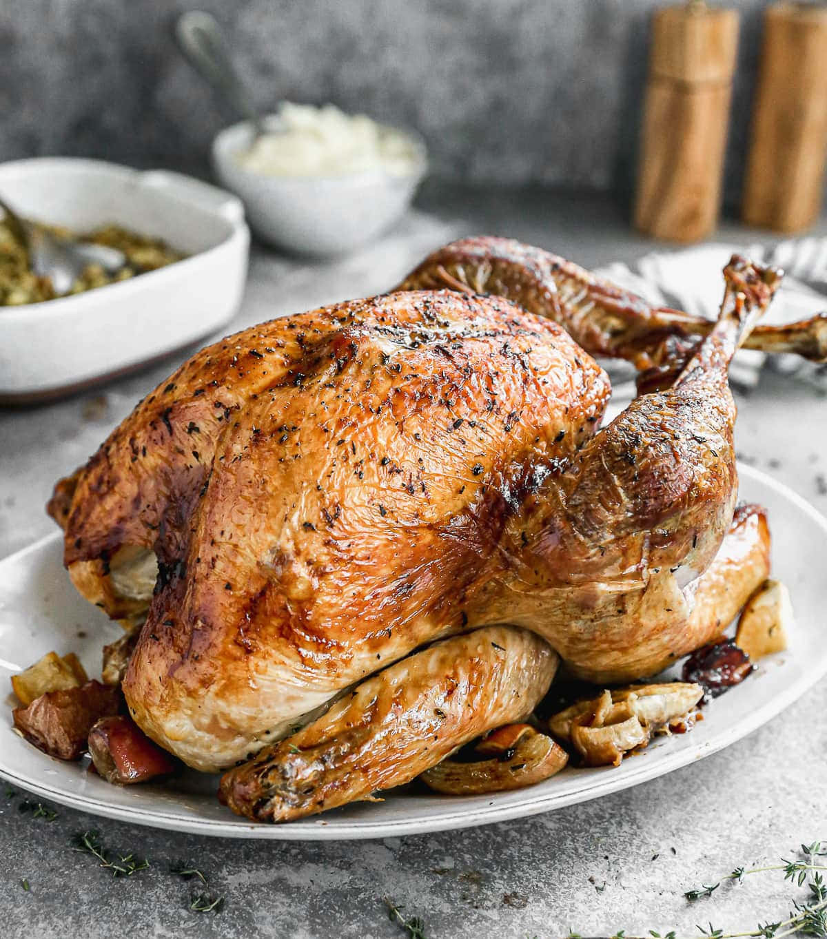 Turkey Happy Thanksgiving 桌布 壁紙 — 一隻金黃色的烤火雞，皮脆肉嫩，放在白色托盤上，周圍環繞著烤蔬菜和新鮮香草。