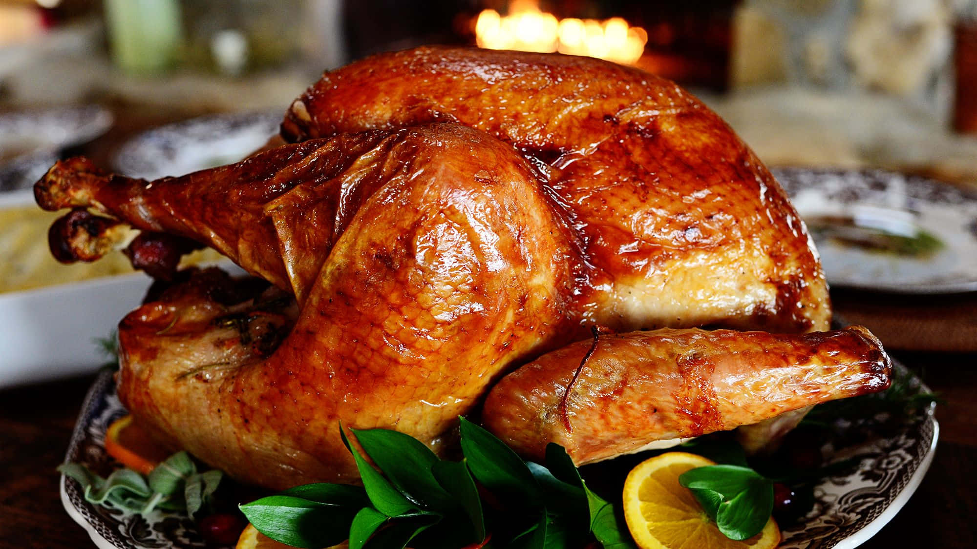 Turkey Happy Thanksgiving 桌布 壁紙 — 一隻金黃色的烤火雞在帶有圖案的托盤上閃爍著肉汁，並以香草和柑橘裝飾。