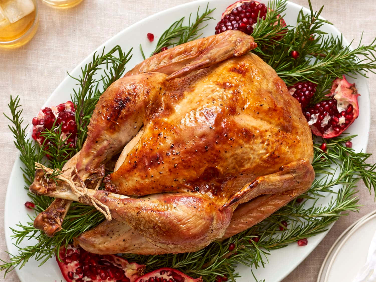 Turkey Happy Thanksgiving 桌布 壁紙 — 一隻金黃色的烤火雞放在白色托盤上，底下鋪著迷迭香和石榴籽。