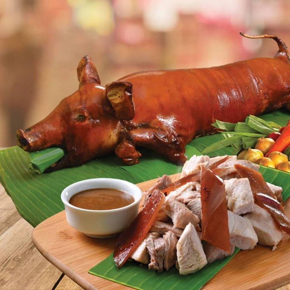 Pig 桌布 壁紙 — 一隻金黃酥脆的烤全豬躺在香蕉葉上，旁邊木板上放著切碎的肉和蘸醬。