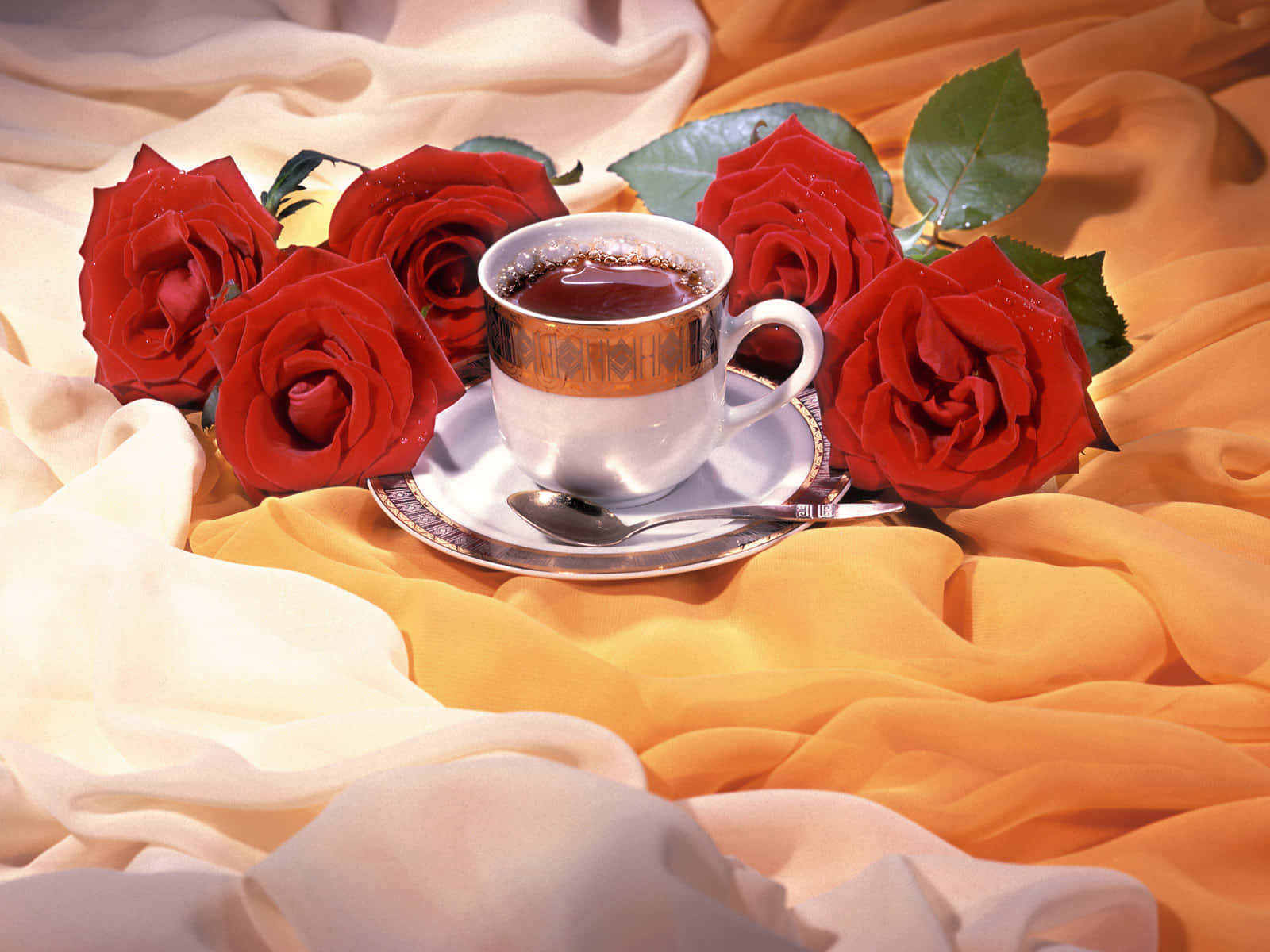 Floral Tea 桌布 壁紙 — 一隻銀色咖啡杯放在碟子上，旁邊是鮮豔的紅玫瑰，襯托著流動的奶油色和金色布料。
