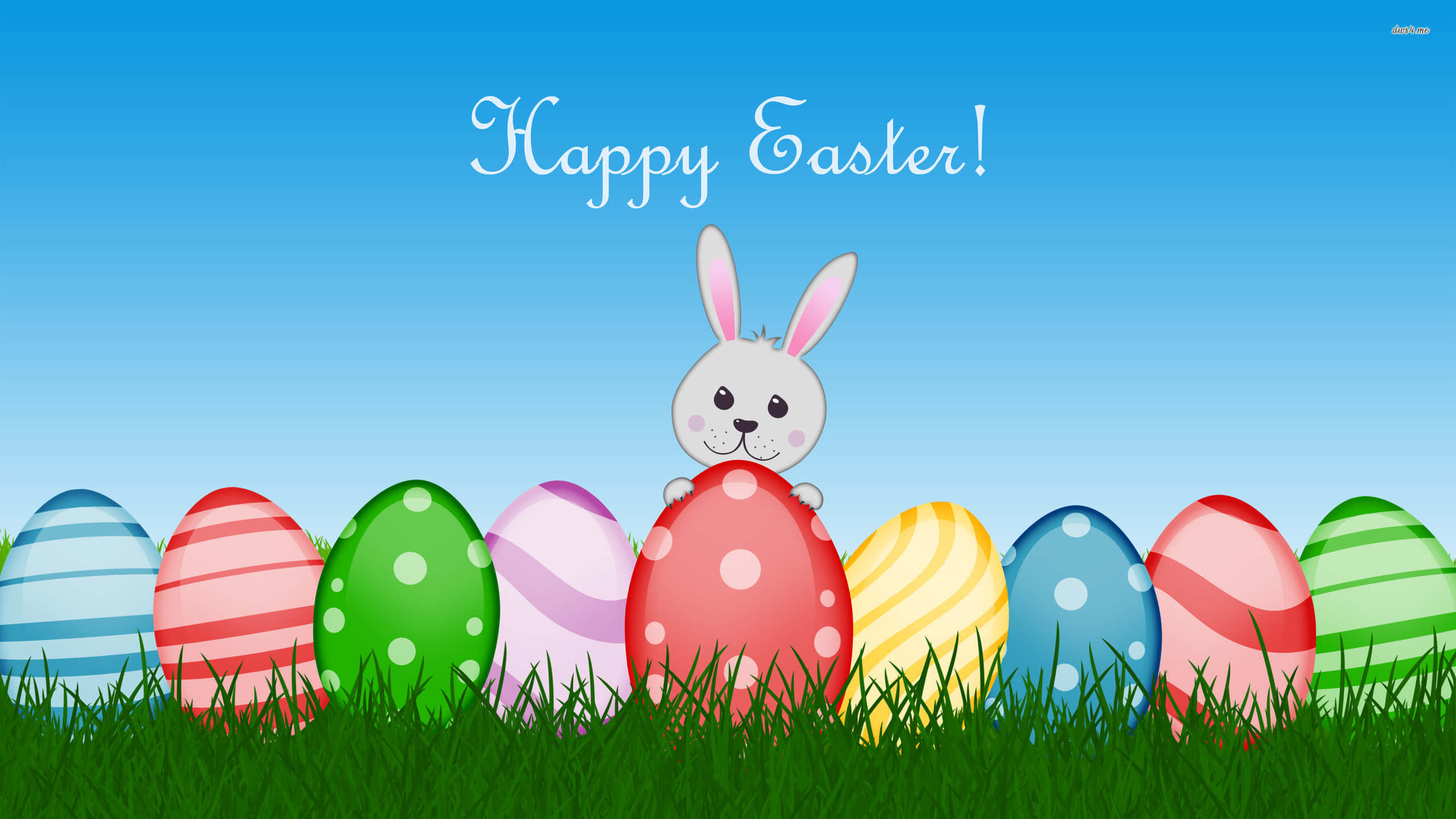 Cute Happy Easter 桌布 壁紙 — 一隻開心的卡通兔子從色彩繽紛的復活蛋後面探出頭來，蛋兒們躺在鮮綠的草地上，背景是晴朗的藍天。