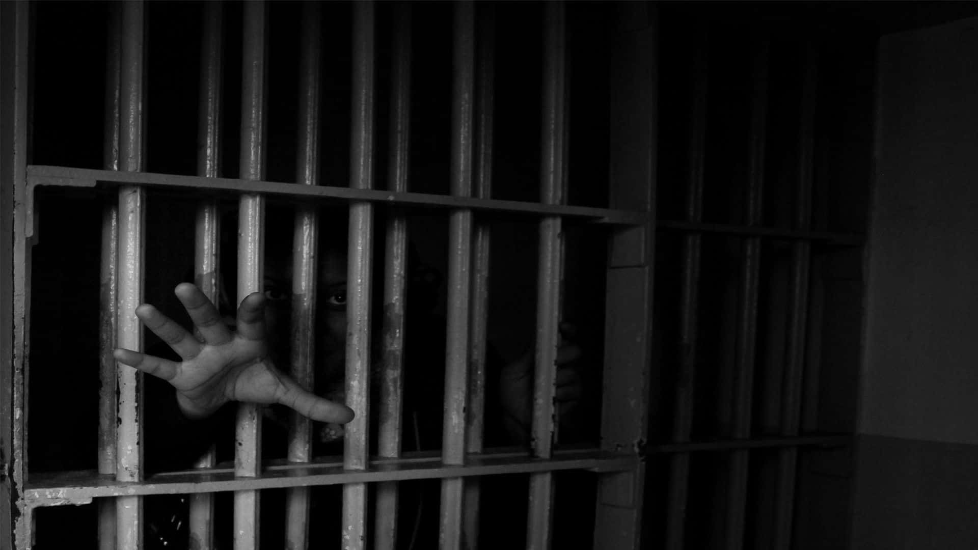 Prison Cell 桌布 壁紙 — 一隻陰影般的手按壓在監獄鐵欄上，一張臉在強烈的黑白對比中窺視出來。