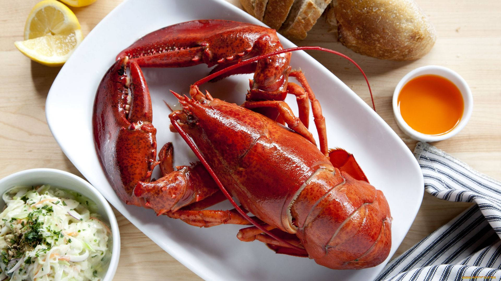Lobster 桌布 壁紙 — 一隻鮮紅色的熟龍蝦放在白色盤子上，周圍有檸檬奶油醬、涼拌高麗菜絲和脆皮麵包，置於木桌上。