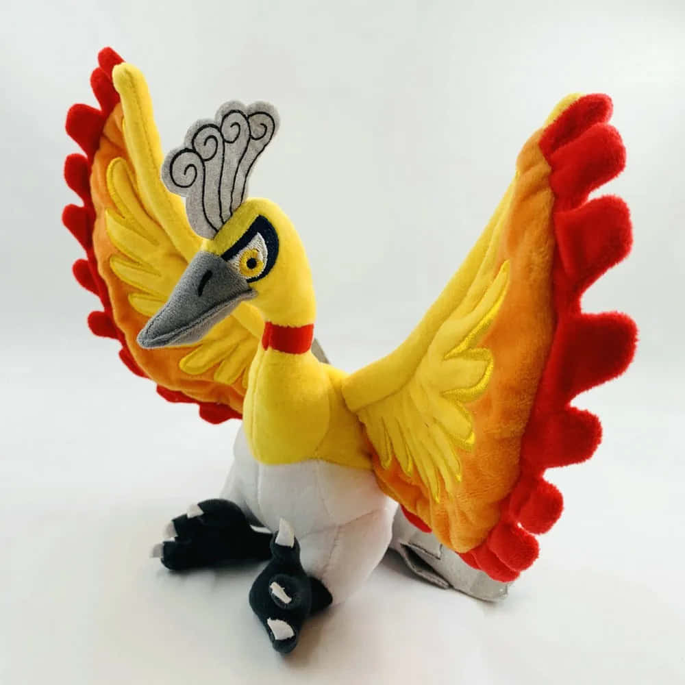 寶可夢 桌布 壁紙 — 一隻鮮豔的黃色和紅色鳳凰毛絨玩具，展開翅膀，帶有精緻的刺繡特徵，擺放在純白色背景前。