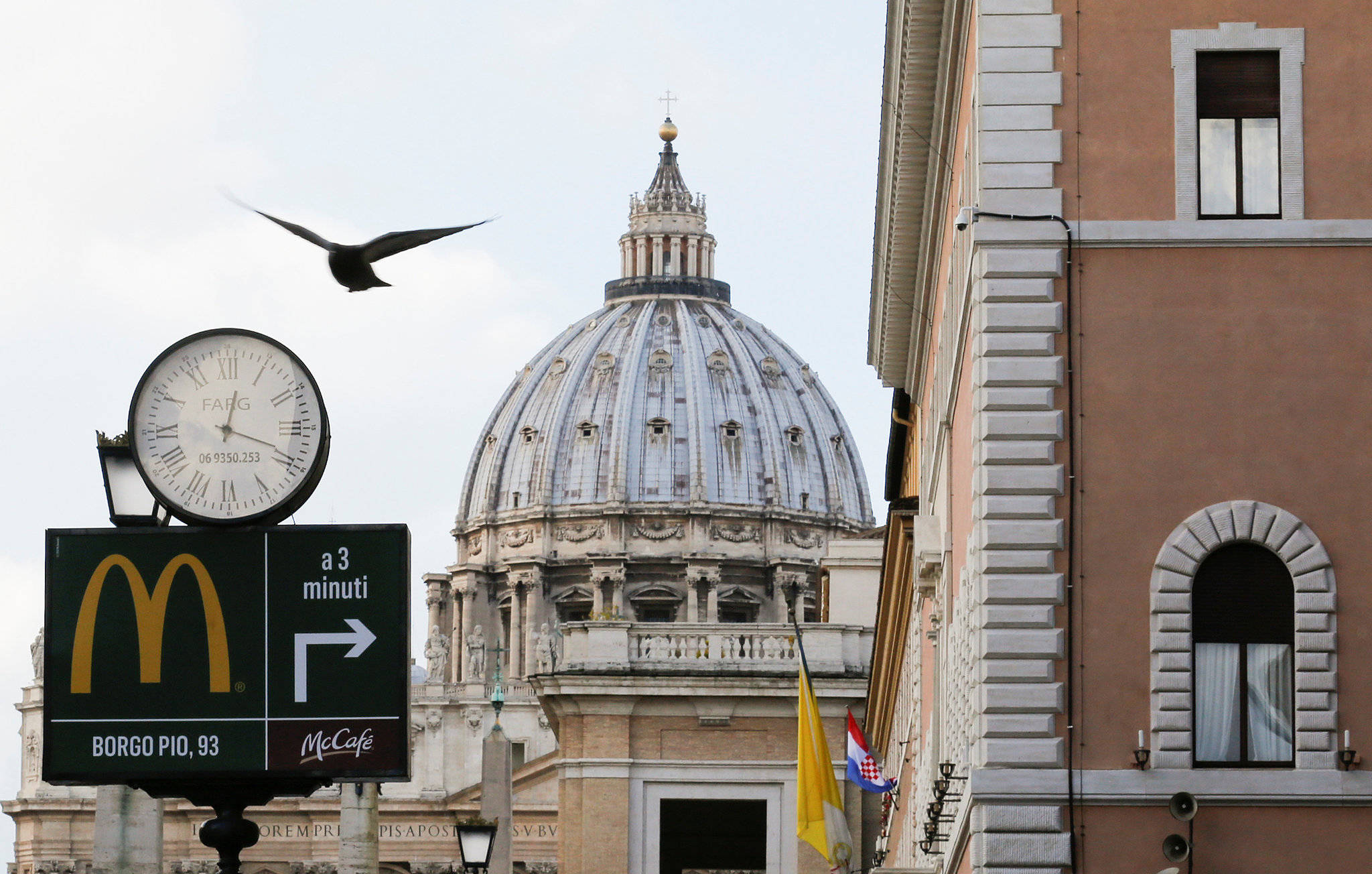 Rome 桌布 壁紙 — 一隻鳥飛過麥當勞的招牌，招牌上有時鐘和箭頭指向博爾戈皮奧，背景是聖彼得大教堂的圓頂。