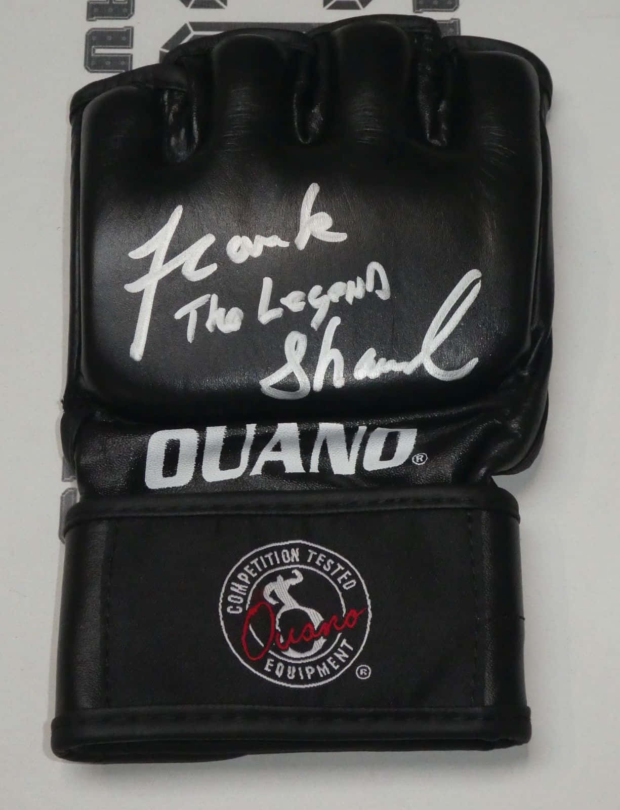 MMA 桌布 壁紙 — 一隻黑色Ouano MMA手套，以銀色簽有「Frank The Legend Shaw」，背景為純白色。