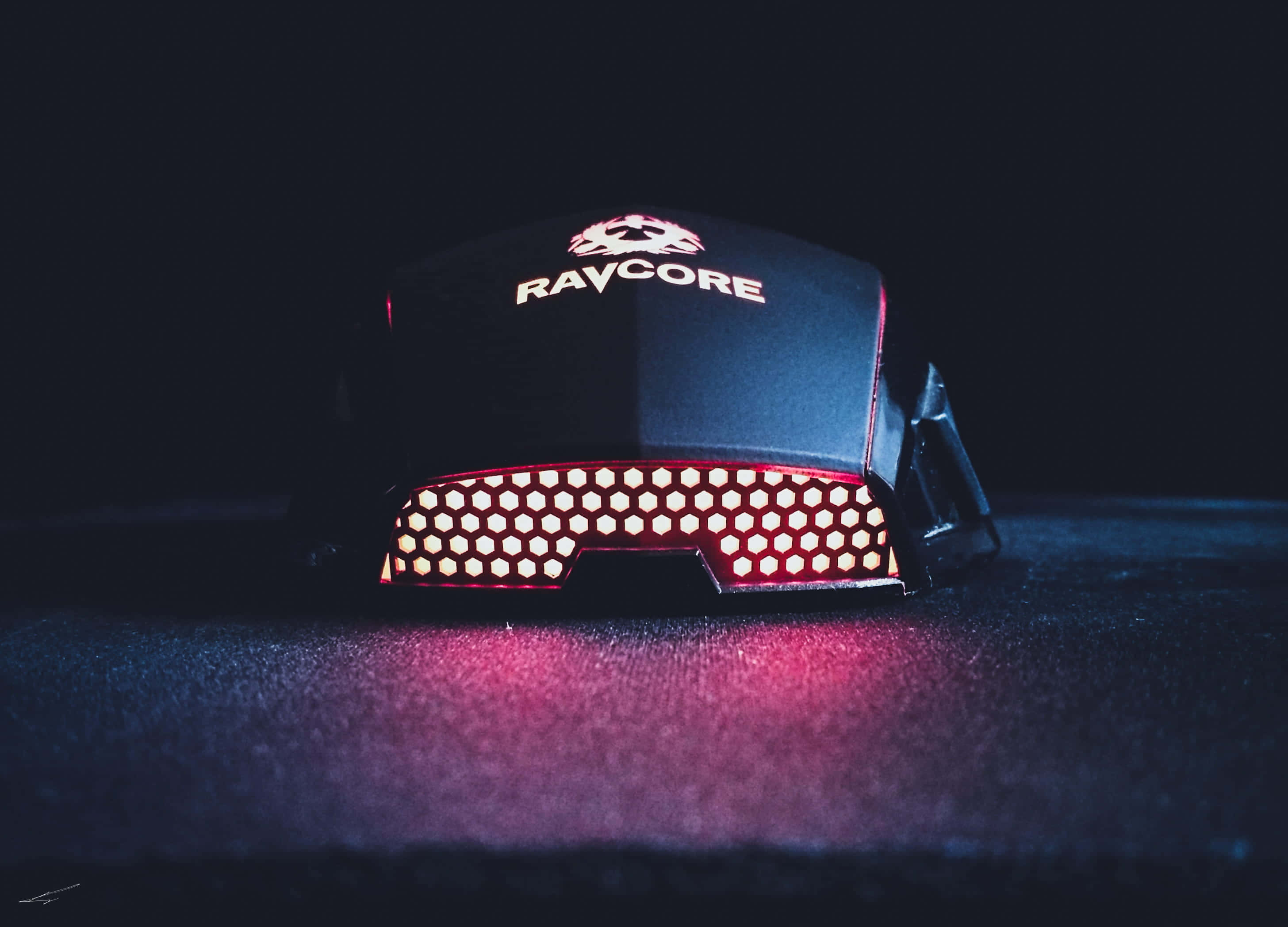 Gaming Mouse 桌布 壁紙 — 一隻黑色RAYCORE電競滑鼠，帶有發光的紅色六角形LED燈，放置在戲劇性燈光下的深色紋理表面上。