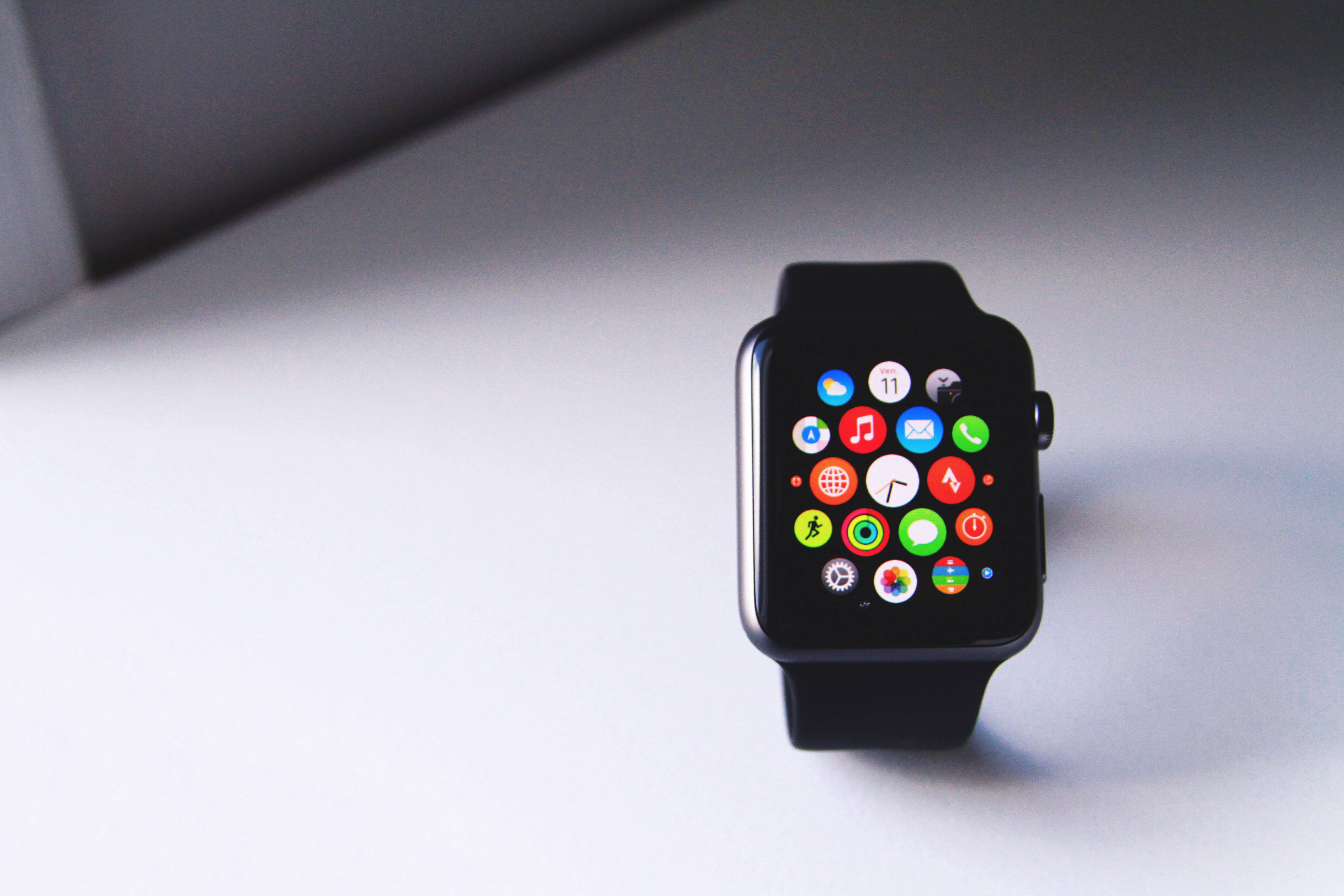 Apple Watch 動態 桌布 壁紙 — 一隻黑色智慧手錶帶有彩色應用程式圖標，放在簡約白色表面上，光線柔和。