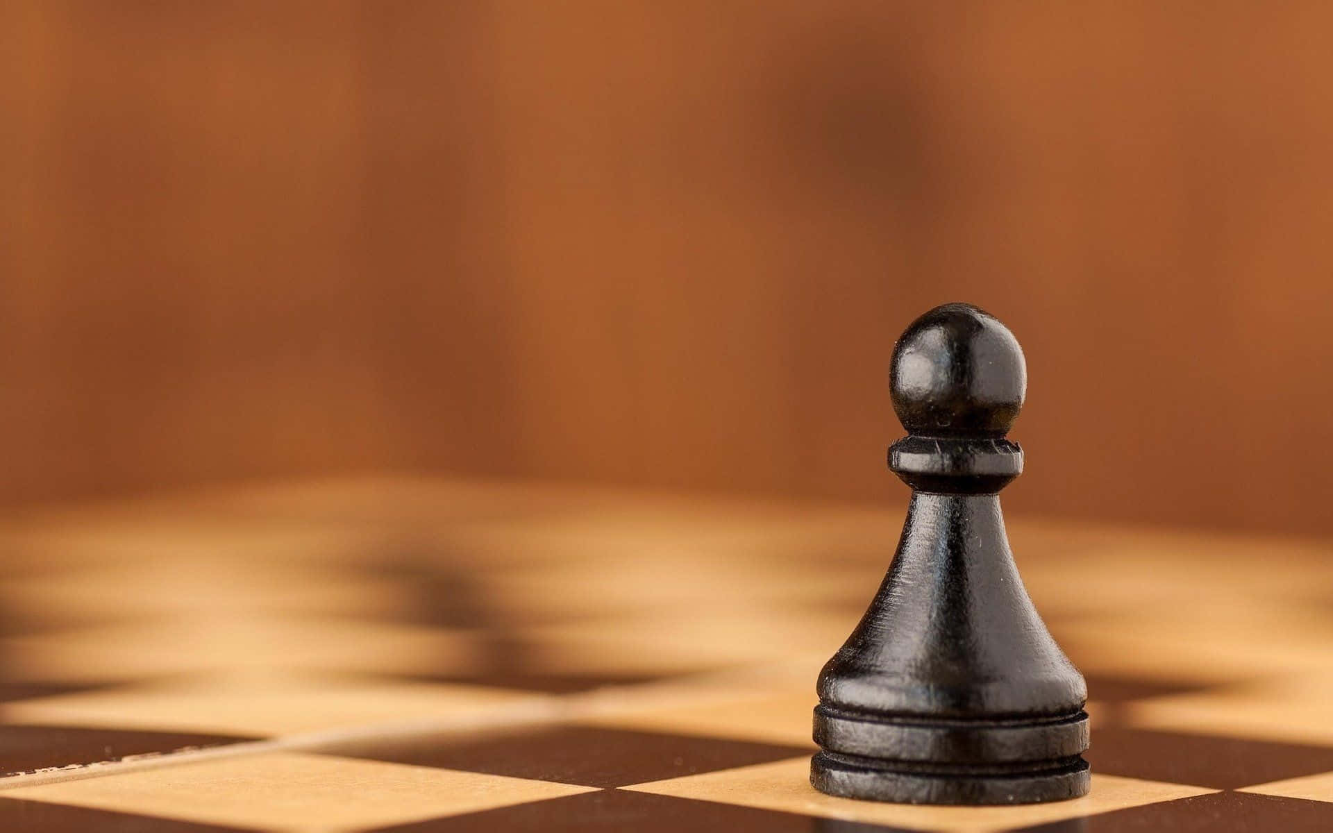 西洋棋 桌布 壁紙 — 一隻黑色西洋棋兵卒清晰地聚焦在木製棋盤上，背景溫暖模糊。