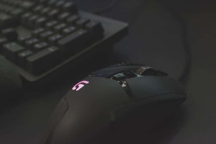 Mouse 桌布 壁紙 — 一隻黑色電競滑鼠帶有發光粉紅色標誌，在昏暗燈光下放在深色書桌上，旁邊有一個鍵盤。