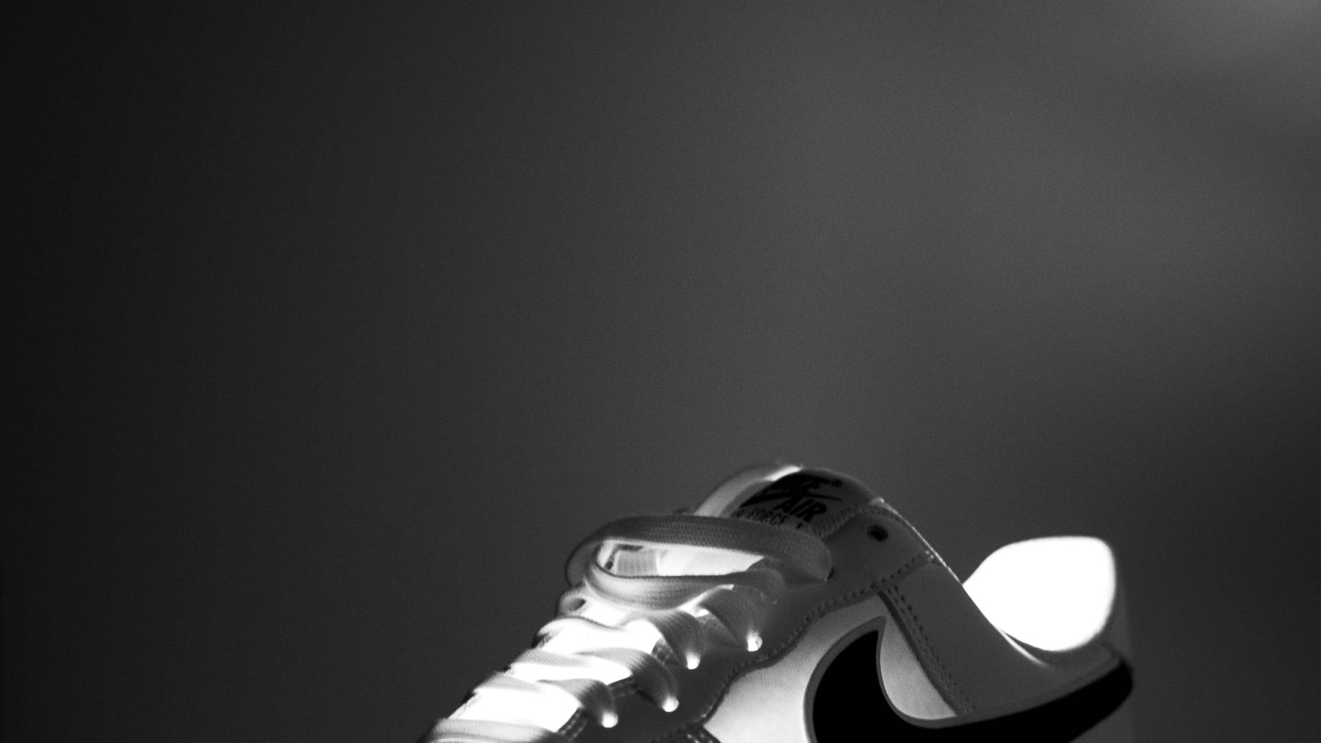 Nike iPhone 桌布 壁紙 — 一雙Nike Air運動鞋在深色漸變背景上，由戲劇性背光照射的黑白特寫。