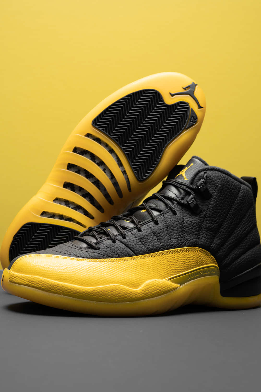 Yellow Jordan 桌布 壁紙 — 一雙大膽的黑黃色Jordan 12運動鞋，展示在鮮豔的黃色背景上，一隻鞋直立，另一隻展示鞋底。