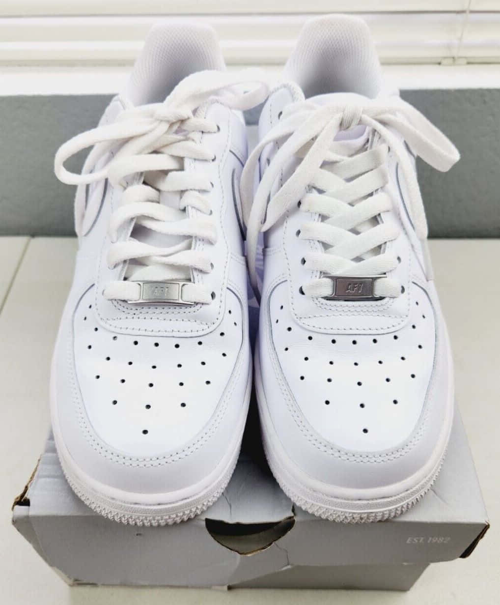 Nike Air Force 桌布 壁紙 — 一雙完美無瑕的白色AF1運動鞋，帶有銀色點綴，放在原裝鞋盒上，背景是中性瓷磚。