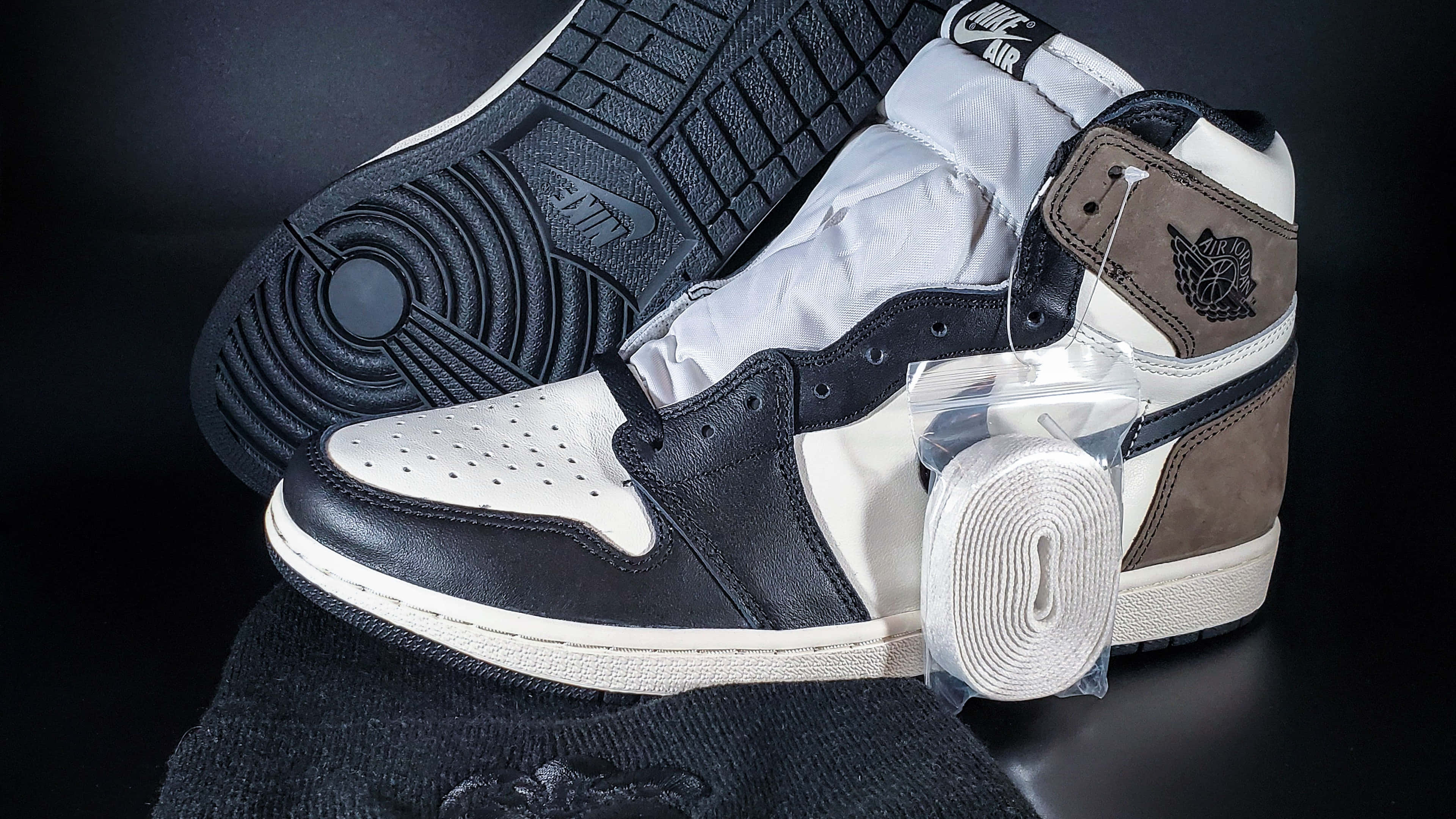 4K 桌布 壁紙 — 一雙完美無瑕的黑白 Air Jordan 1 運動鞋，帶有棕色點綴，未包裝地放置在深色表面上，展示其標誌性設計和簡潔線條。