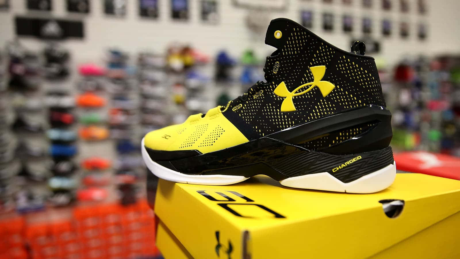 Under Armour 桌布 壁紙 — 一雙帶有 'CHARCOAL' 字樣的黑色和黃色 Under Armour 籃球鞋，放在其匹配的黃色鞋盒上，位於光線明亮的運動鞋店內。
