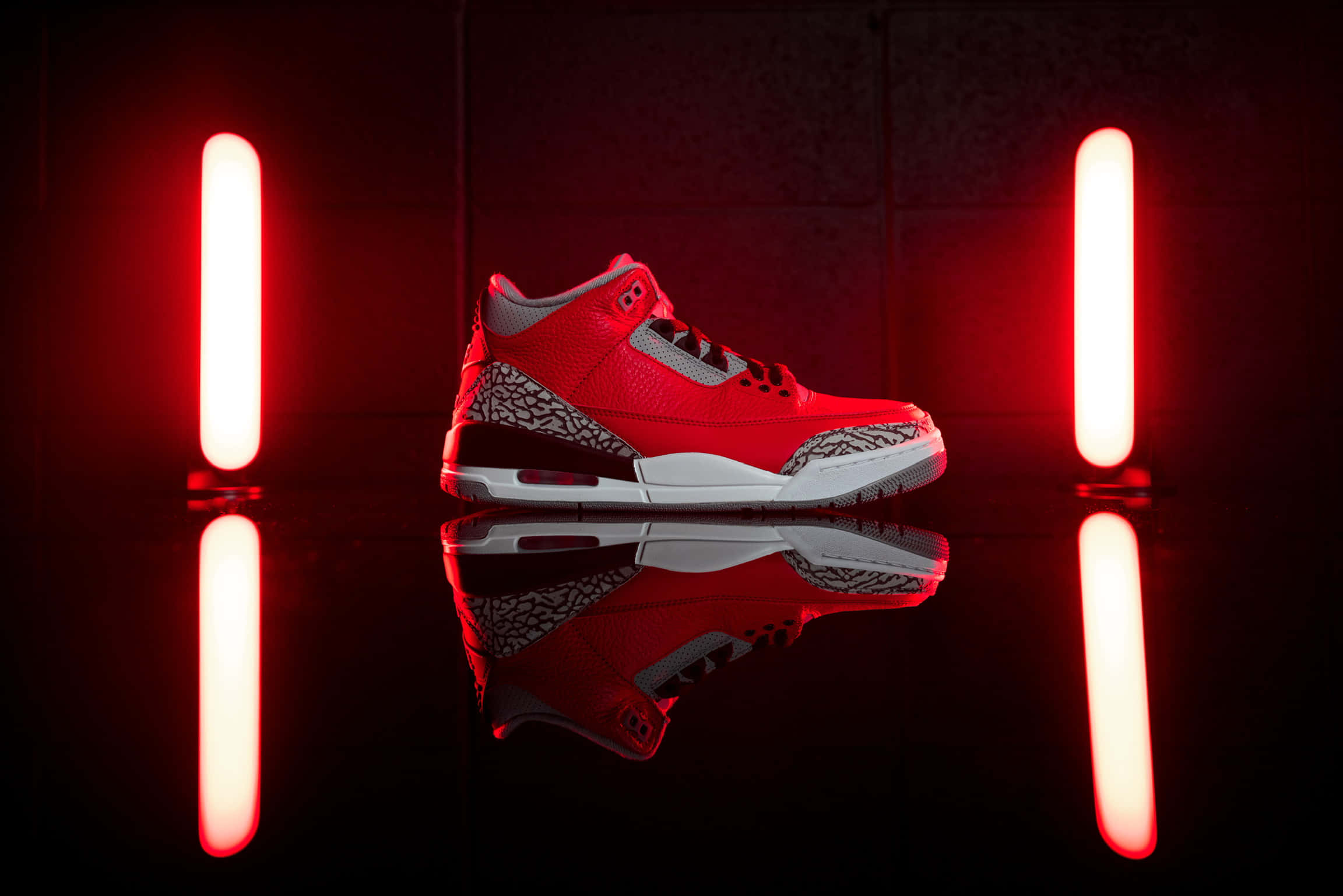 Red Shoes 桌布 壁紙 — 一雙帶有大象紋細節的紅色 Jordan 3 運動鞋，在反光的黑色表面上，居中於發光的紅色霓虹燈管之間。