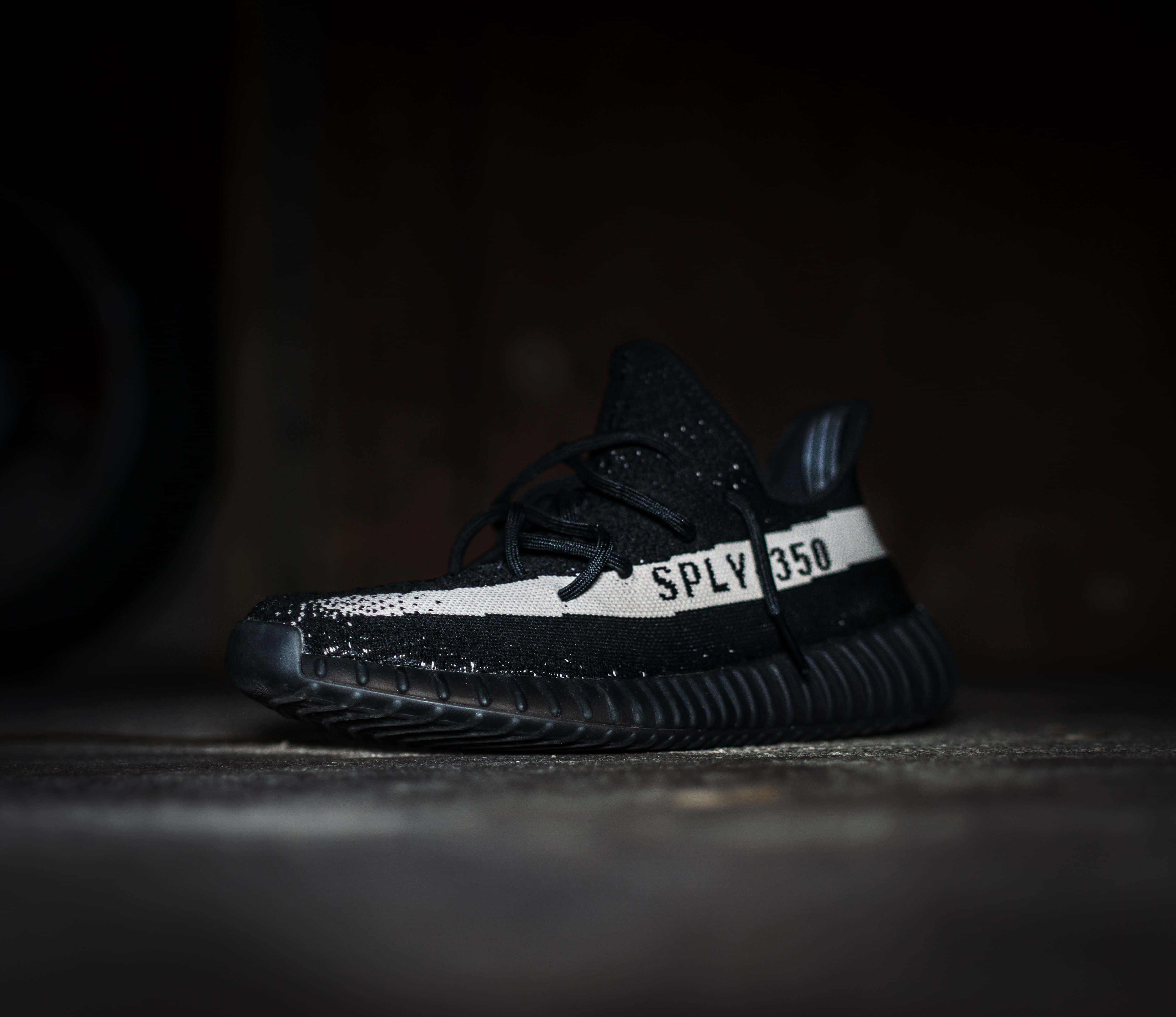 鞋子 桌布 壁紙 — 一雙帶有白色條紋和「SPLY 350」字樣的黑色Yeezy Boost 350運動鞋，在昏暗光線下放在混凝土地板上。