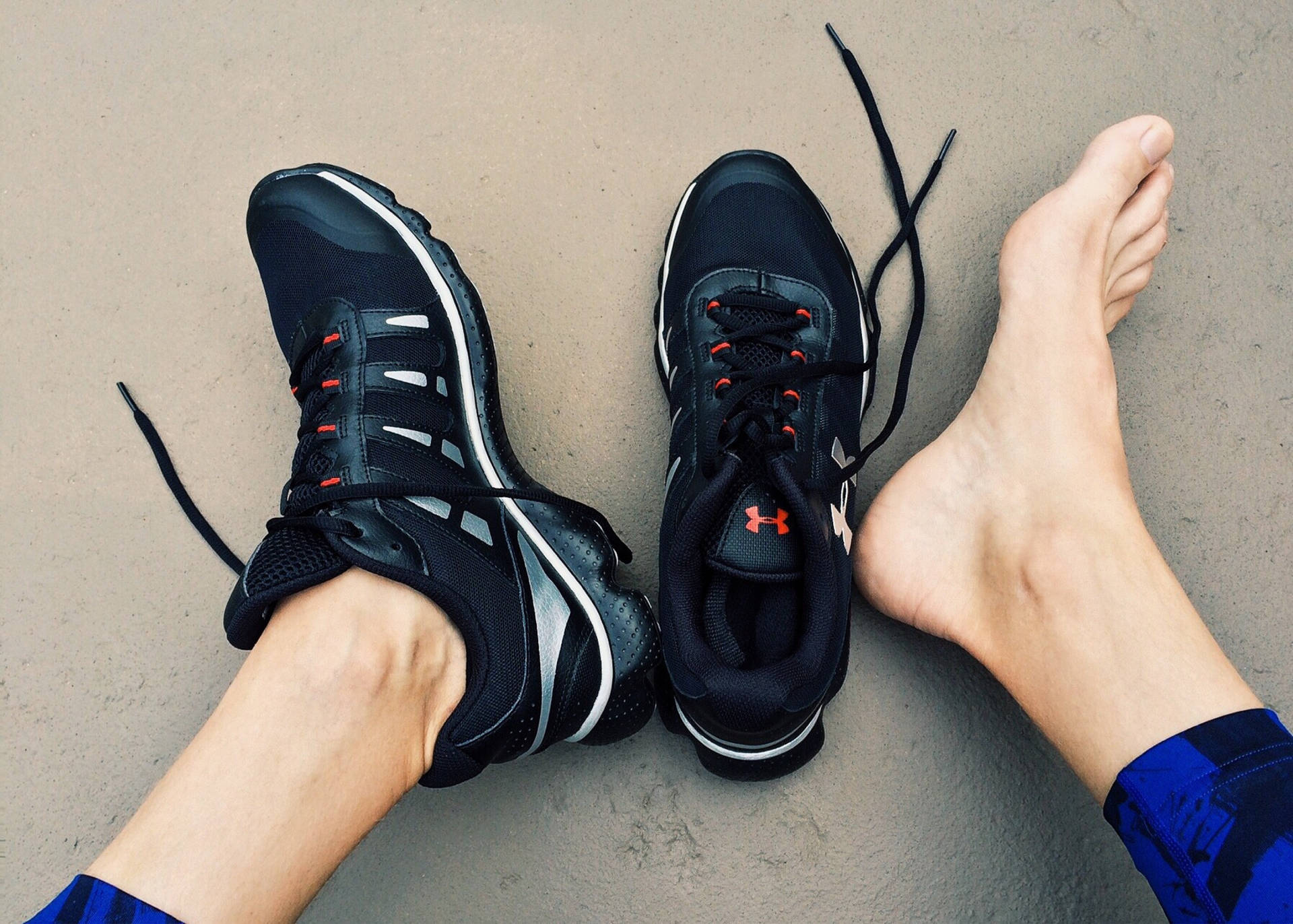 feet 桌布 壁紙 — 一雙帶有紅色點綴的黑色運動鞋放在赤腳旁邊，置於有紋理的灰色表面上。