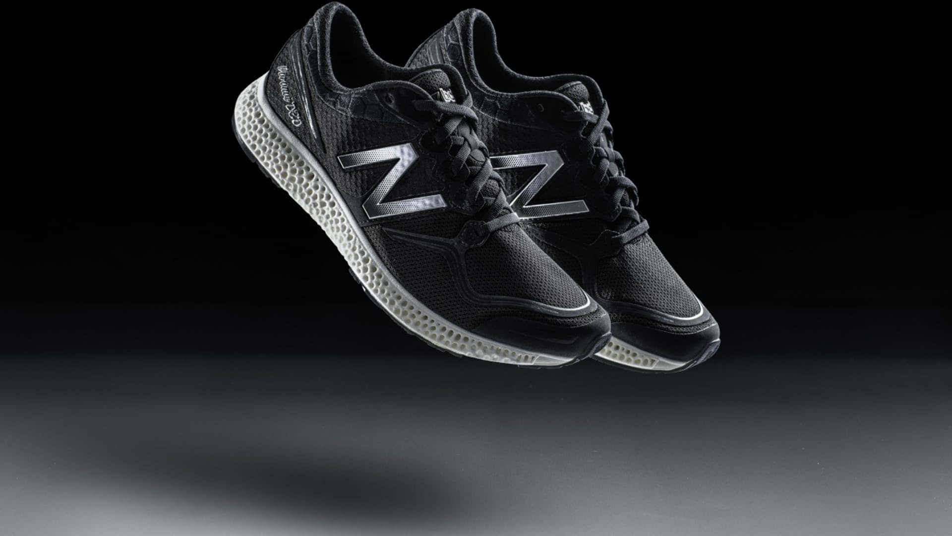 New Balance 桌布 壁紙 — 一雙帶有銀色標誌的黑色New Balance運動鞋在深色漸變背景上漂浮。