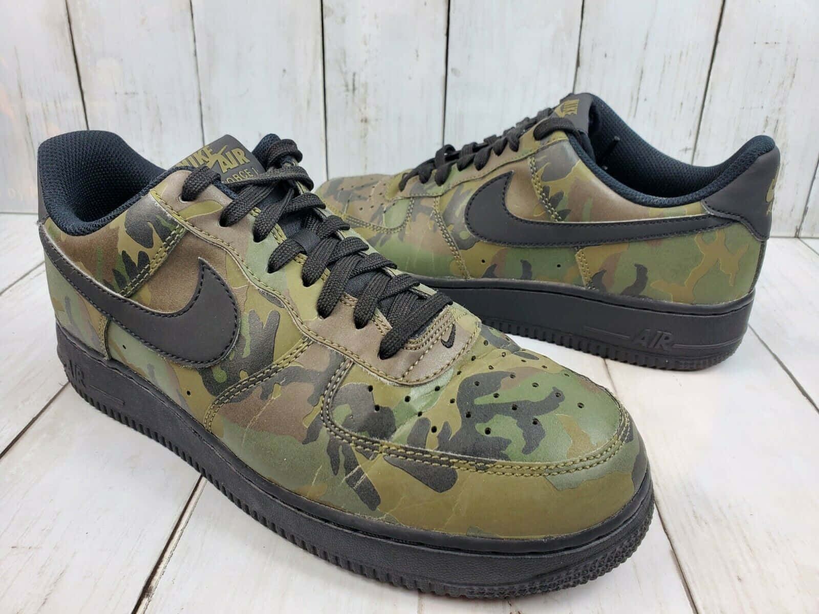 Nike Air Force 桌布 壁紙 — 一雙帶有黑色點綴的迷彩圖案Nike Air Force 1運動鞋放在風化的白色木地板上。