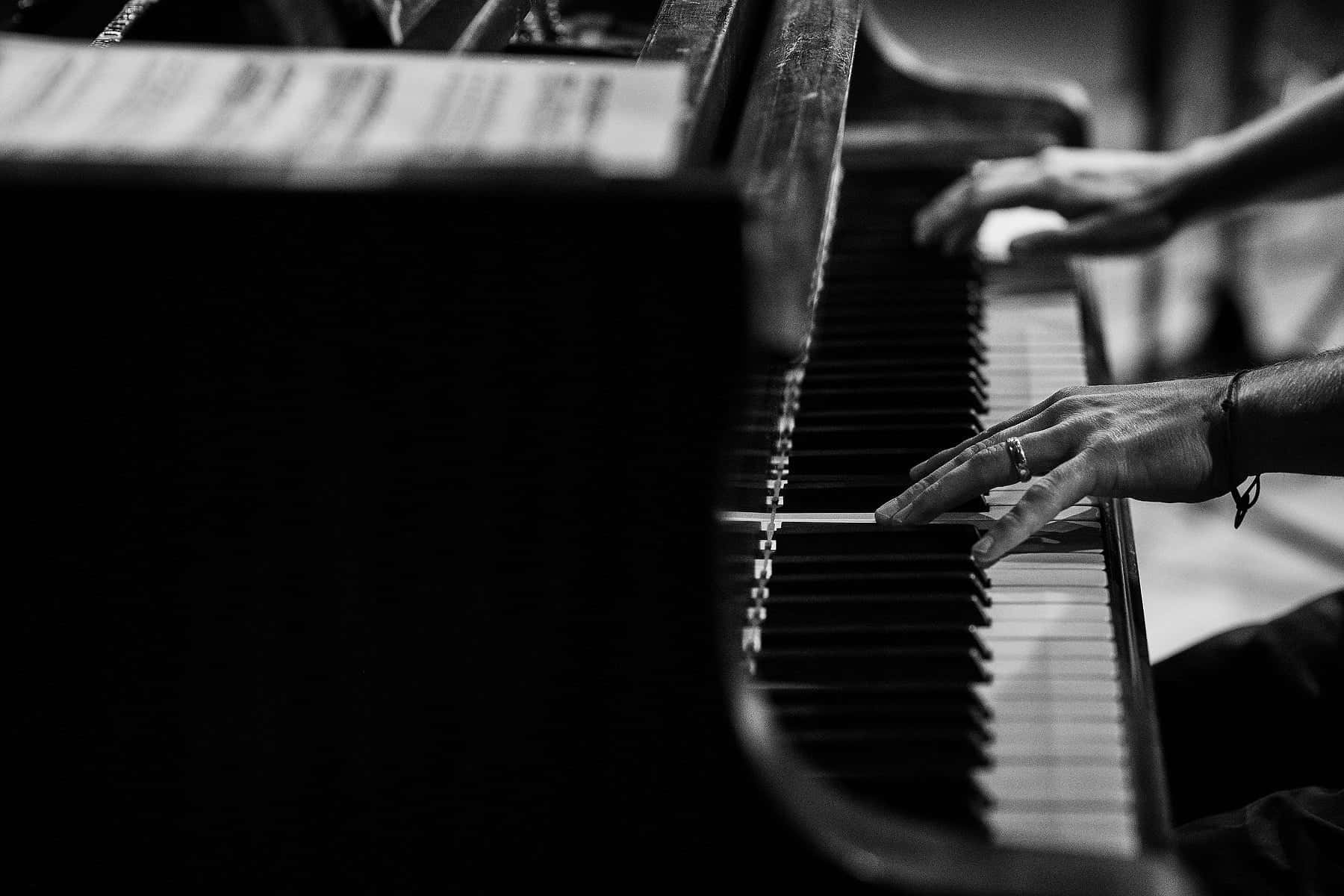 Black And White Piano 桌布 壁紙 — 一雙彈奏三角鋼琴的手的黑白特寫，聚焦於琴鍵和手指。