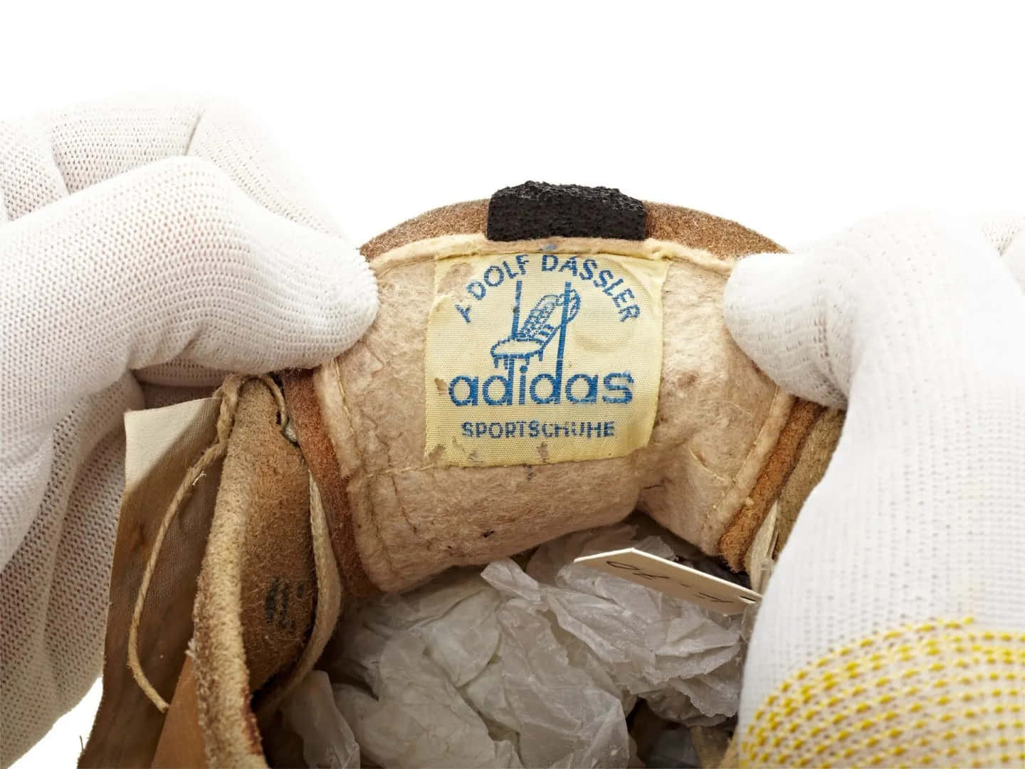 愛迪達 桌布 壁紙 — 一雙戴著手套的手拿著復古Adidas運動鞋標籤，露出其陳舊的皮革內部及原始品牌標誌。