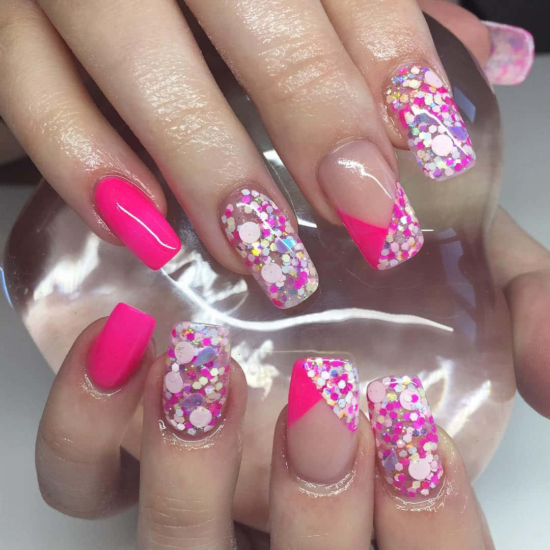 Pink Nail Art 桌布 壁紙 — 一雙手的特寫，帶有充滿活力的粉紅色指甲，飾有彩色亮片和幾何圖案。