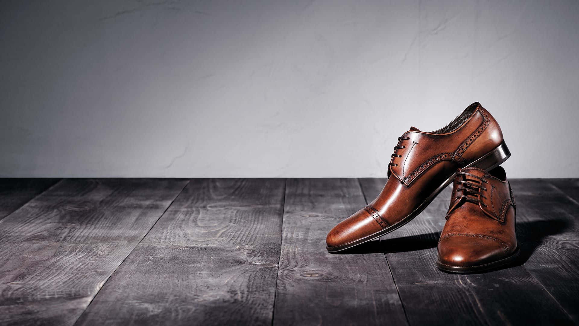 Footwear Design 桌布 壁紙 — 一雙拋光棕色皮革正裝鞋放在深色木板上，背景是帶紋理的灰色牆壁。