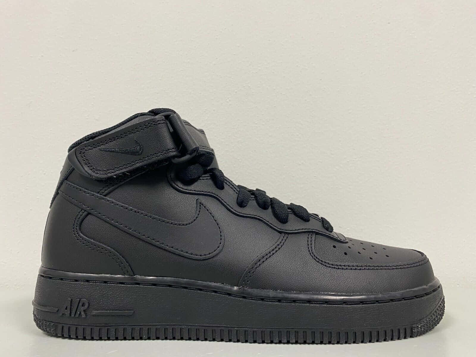 Nike Air Force 桌布 壁紙 — 一雙時尚的全黑色Nike Air Force 1高筒運動鞋，配有魔鬼氈帶和透氣孔鞋頭，置於純白色背景前。