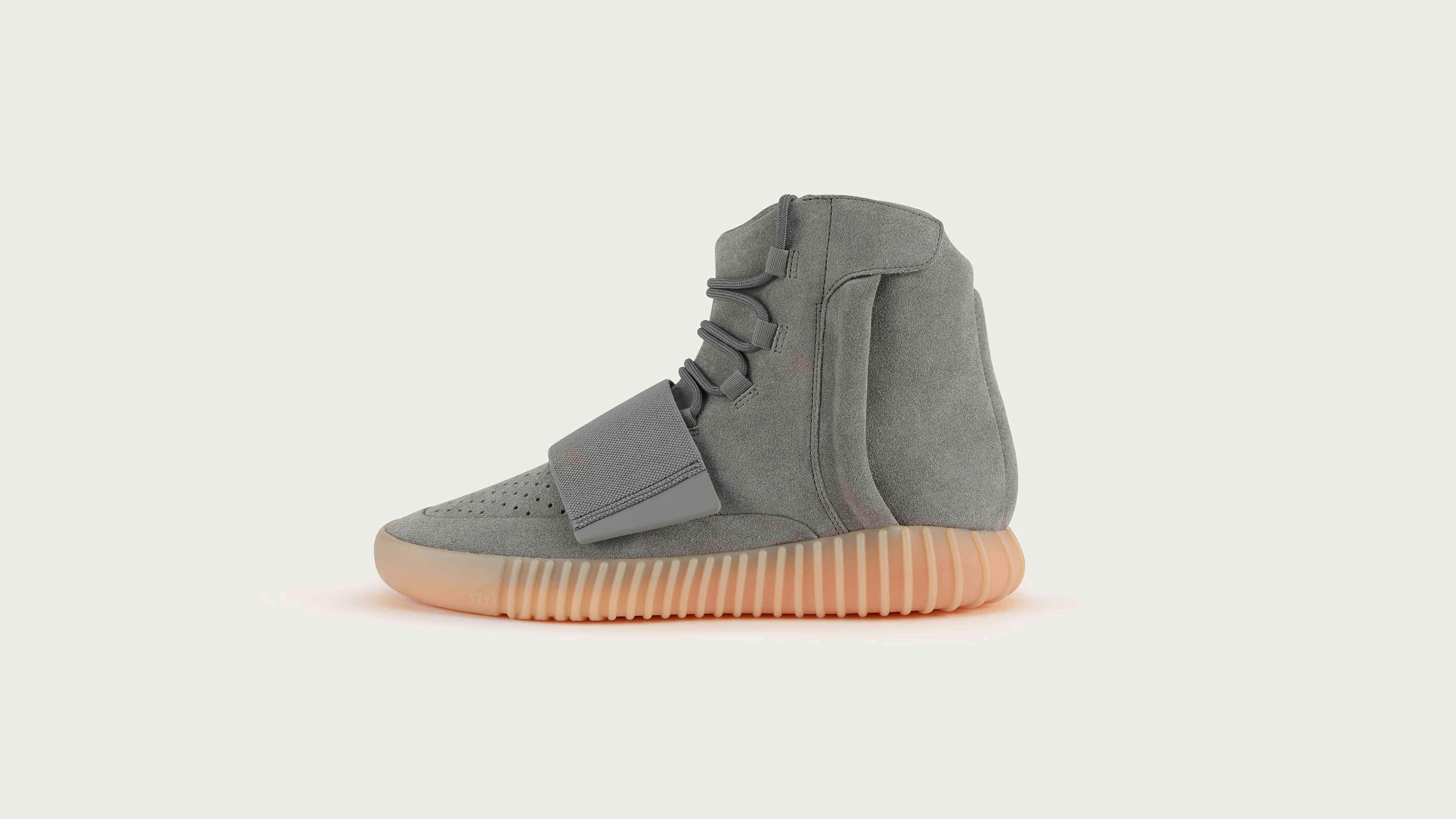 Yeezy 桌布 壁紙 — 一雙時尚的灰色高筒運動鞋，搭配蜜桃色鞋底，孤立地立在柔和的米白色背景上。