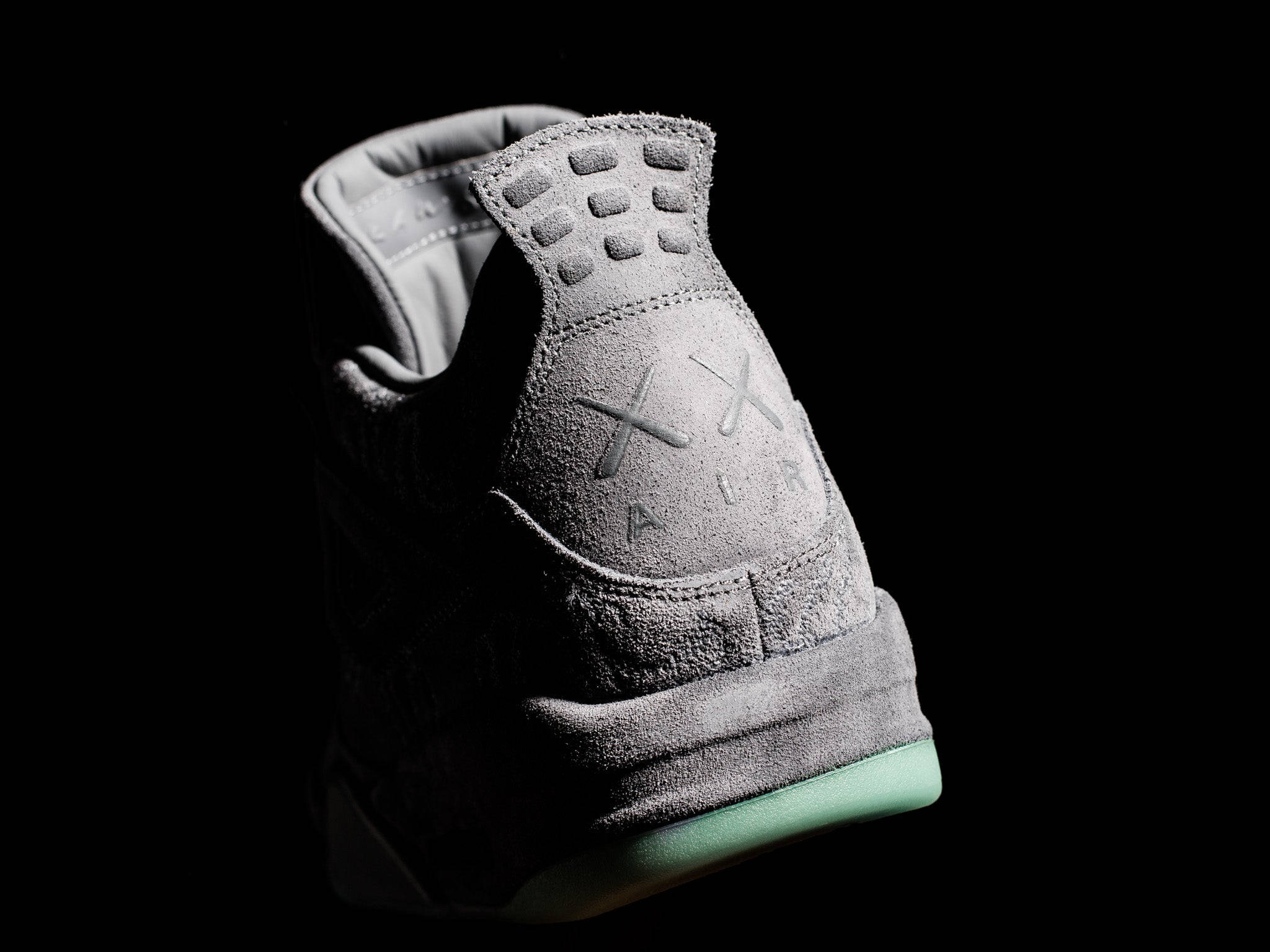 KAWS 桌布 壁紙 — 一雙時尚的灰色麂皮運動鞋，搭配薄荷綠色鞋底，在純黑色背景上閃耀。
