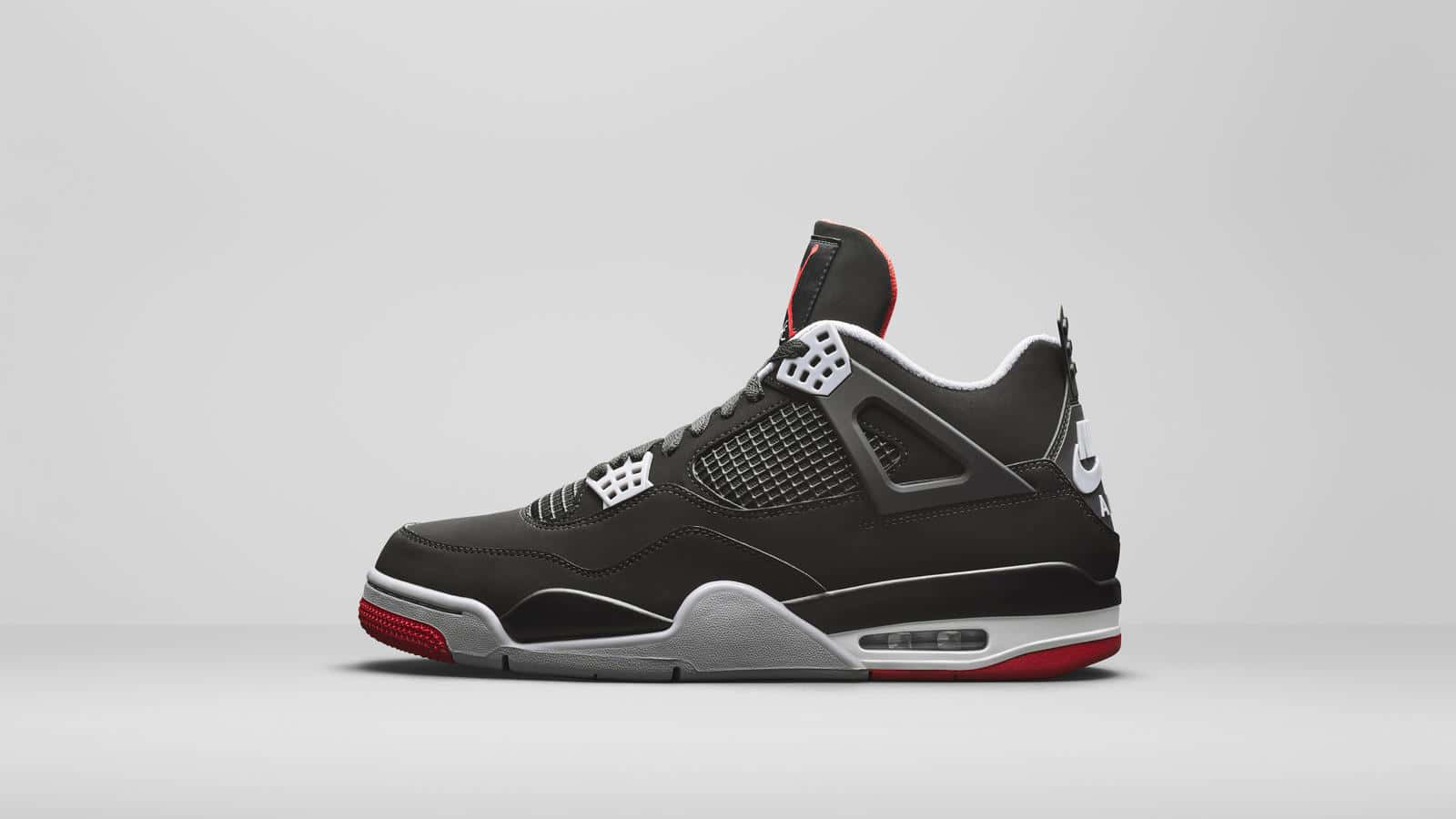 Air Jordan 桌布 壁紙 — 一雙時尚的黑色 Jordan 4 運動鞋，帶有紅色和銀色點綴，以側面姿態立於簡約灰色工作室背景前。
