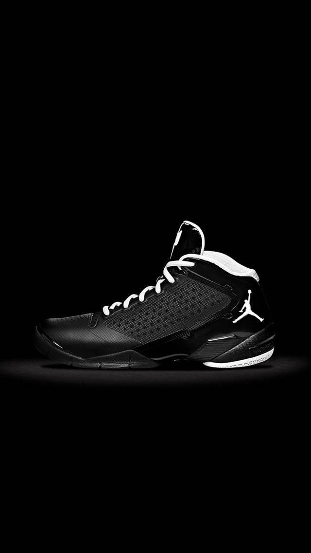 Jordan球鞋 桌布 壁紙 — 一雙時尚的黑色Jordan運動鞋，配有白色鞋帶和Jumpman標誌，在純黑色背景上孤立地站立，並有戲劇性的聚光燈照射。