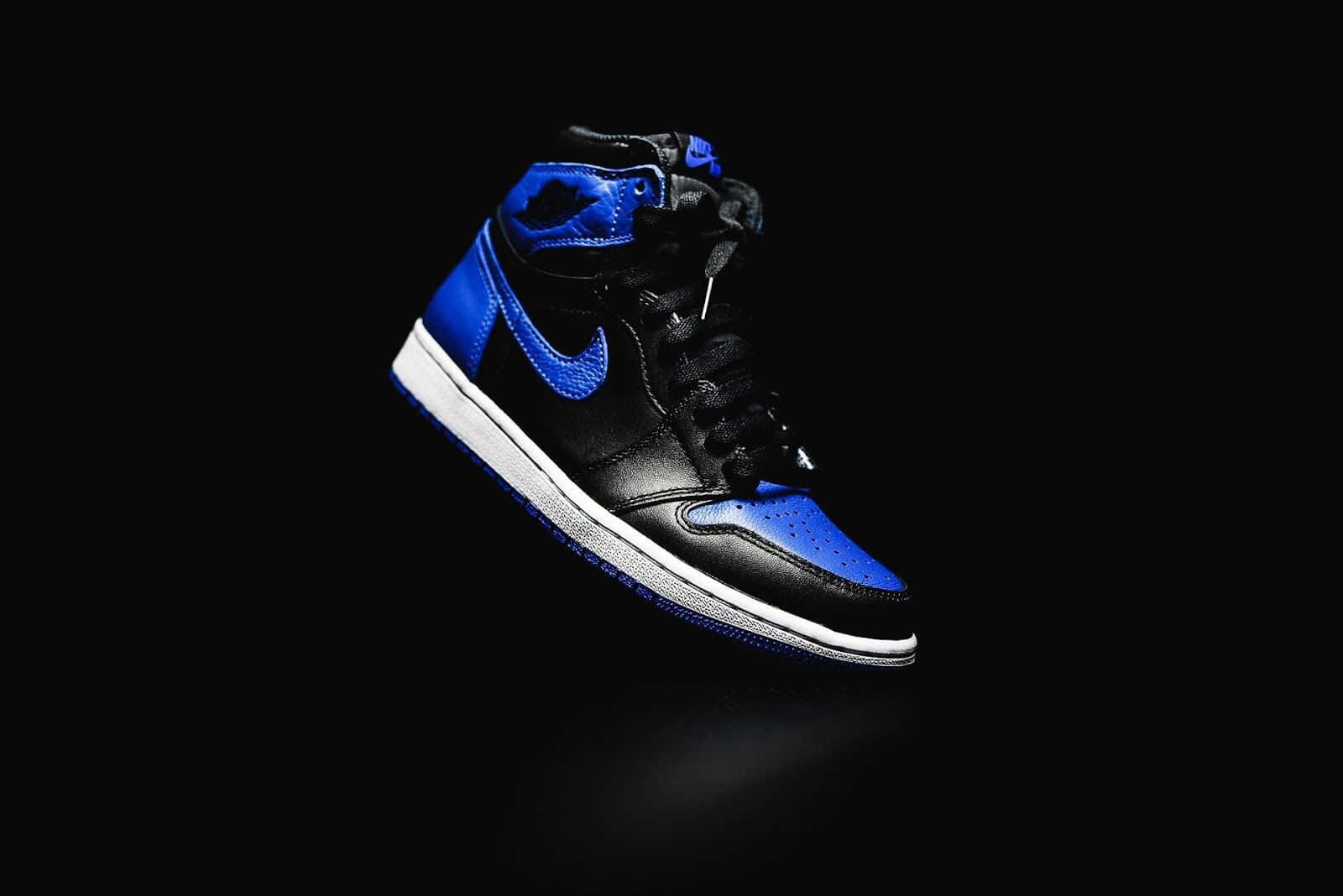 Nike Air Jordan 1 桌布 壁紙 — 一雙時尚的黑色和皇家藍色高筒運動鞋在純黑色背景上漂浮，帶有戲劇性的燈光。