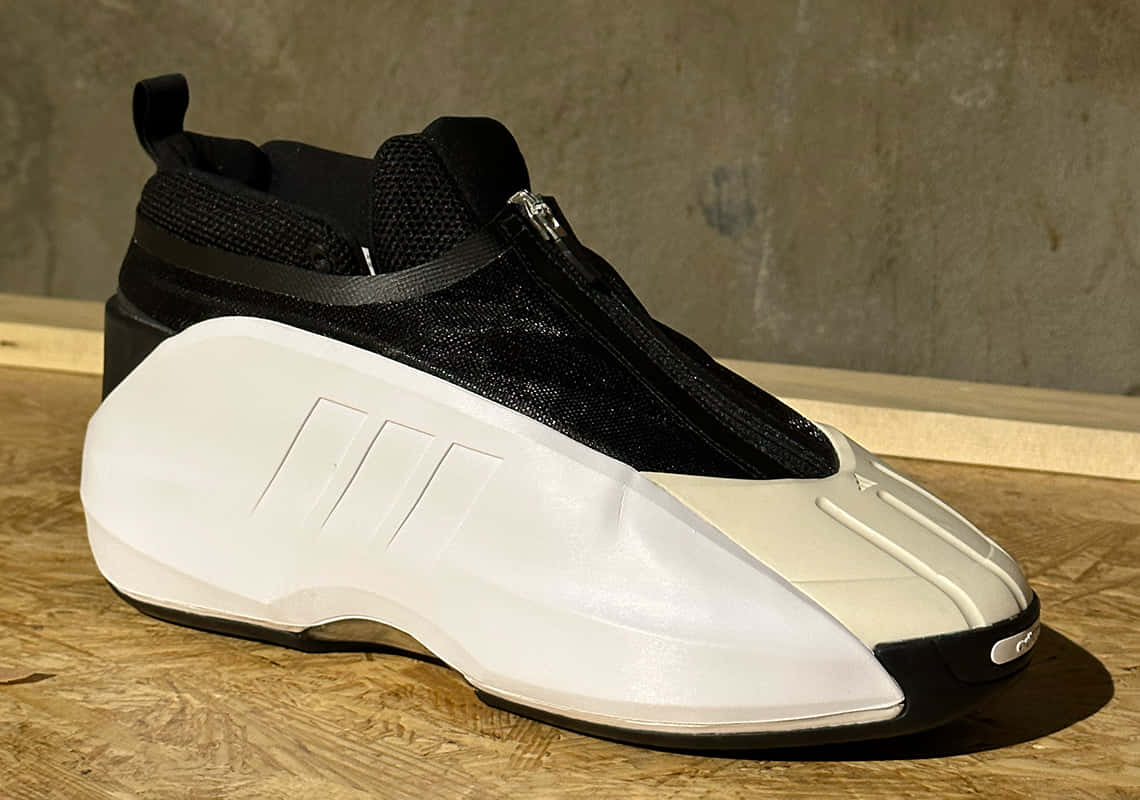 愛迪達 桌布 壁紙 — 一雙未來感黑白運動鞋，帶拉鍊，放在木質表面上，背景是混凝土牆。