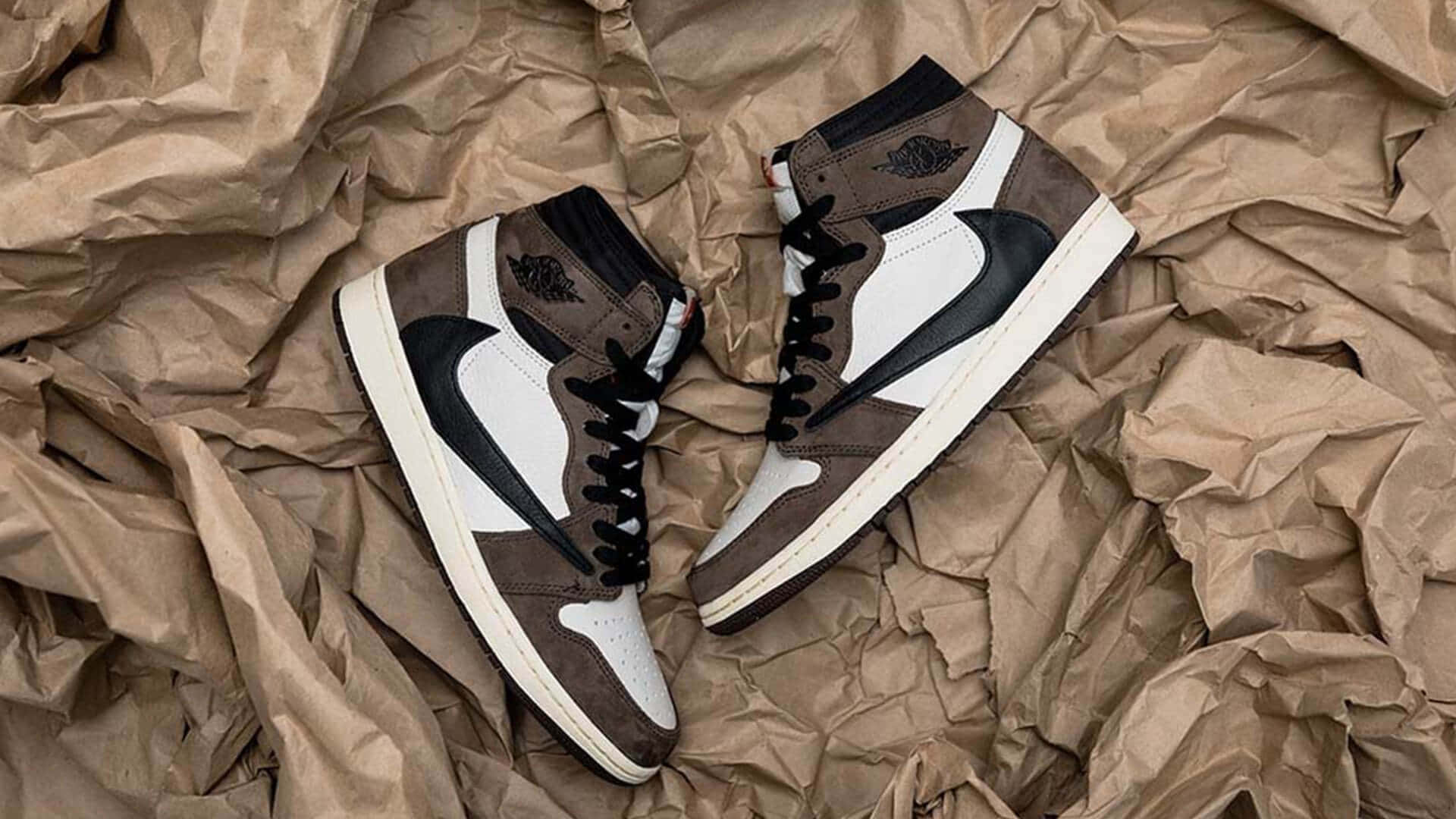 Travis Scott Jordan 1 桌布 壁紙 — 一雙棕色、白色和黑色的高筒運動鞋放在帶有紋理細節的皺巴巴棕色紙上。