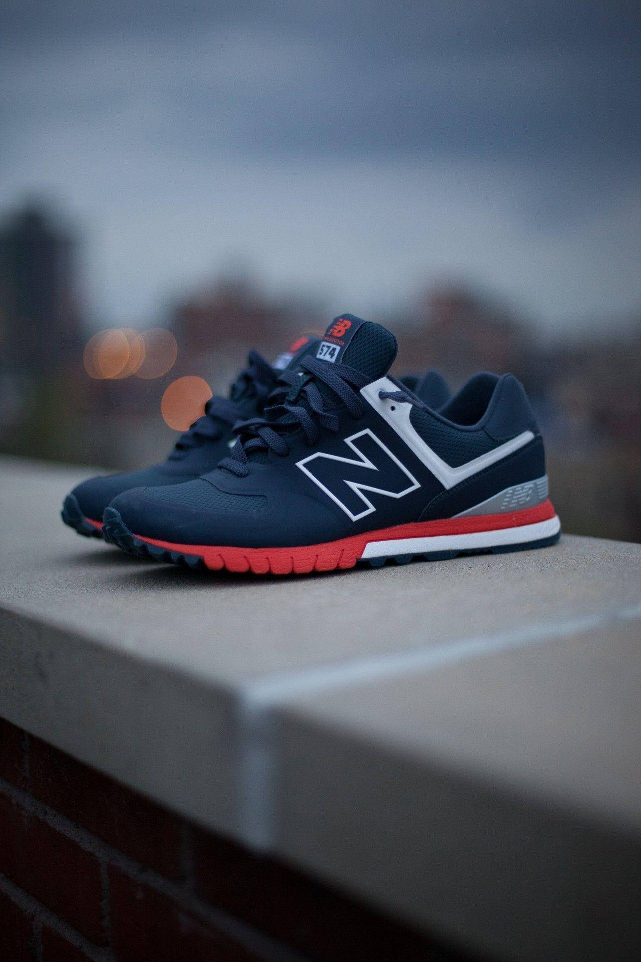 New 桌布 壁紙 — 一雙海軍藍 New Balance 運動鞋（紅色鞋底）在黃昏時分放在混凝土邊緣上，背景是模糊的城市天際線。