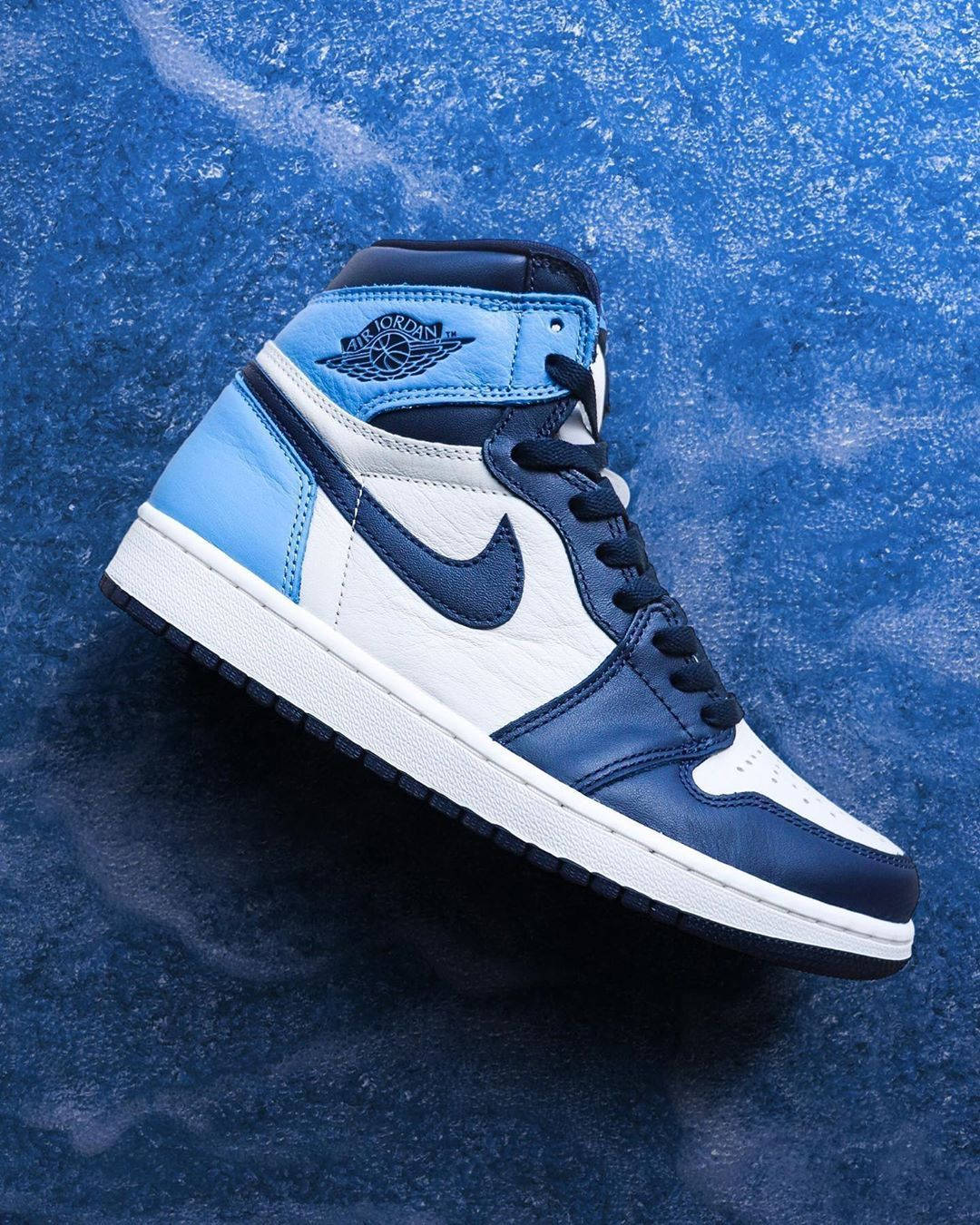 Nike Air Jordan 1 桌布 壁紙 — 一雙海軍藍、淺藍和白色的高筒 Air Jordan 運動鞋放在有紋理的藍色表面上。