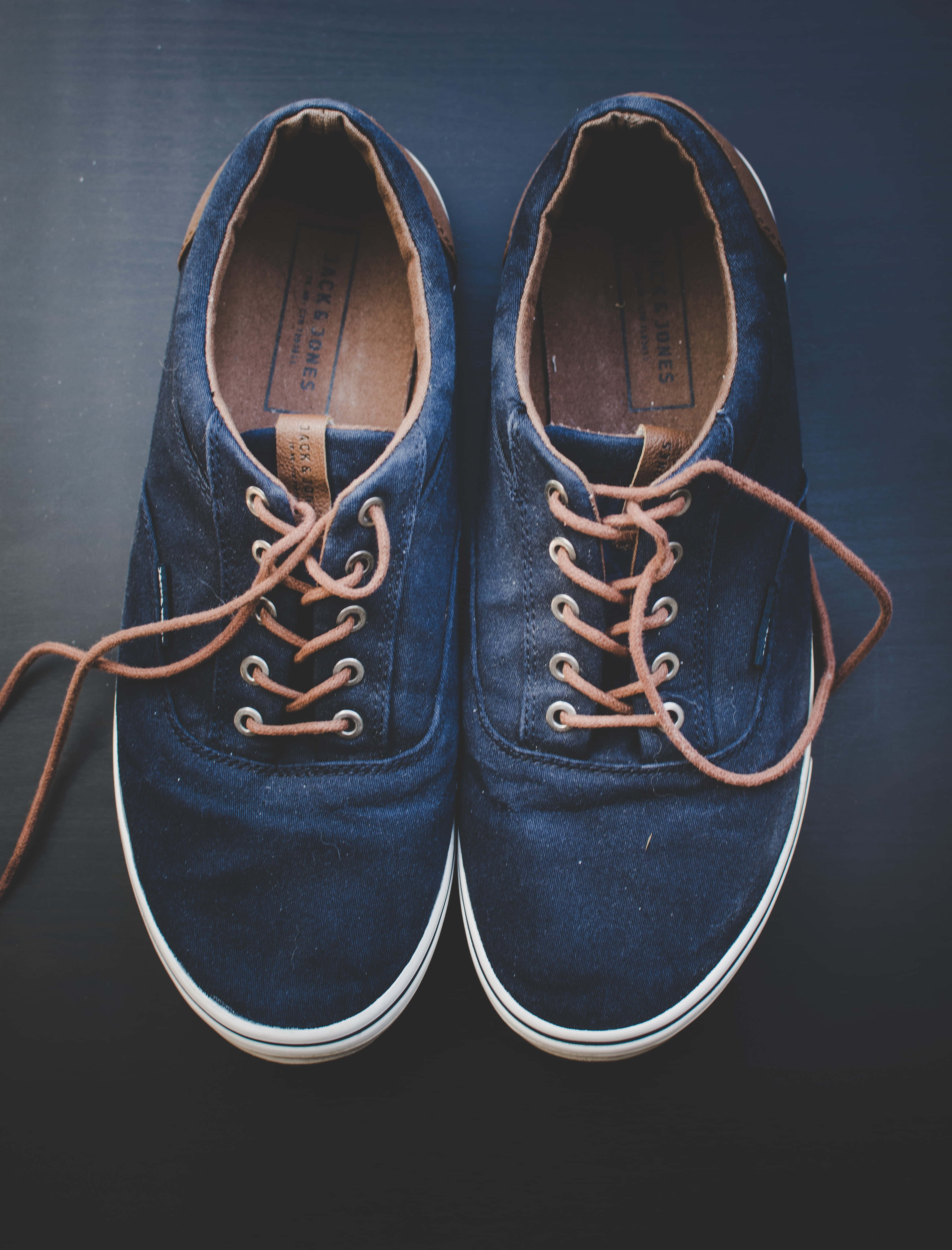 Navy Blue Shoes 桌布 壁紙 — 一雙海軍藍絨面革運動鞋搭配棕褐色鞋帶，放置在深色表面上，展現經典休閒風格。