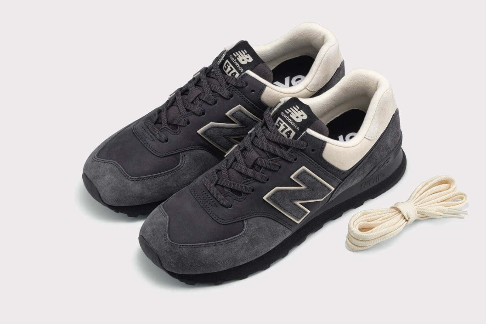 New Balance 桌布 壁紙 — 一雙深灰色麂皮 New Balance 574 運動鞋，帶有奶油色點綴和相配的鞋帶，展示在乾淨的白色背景上。