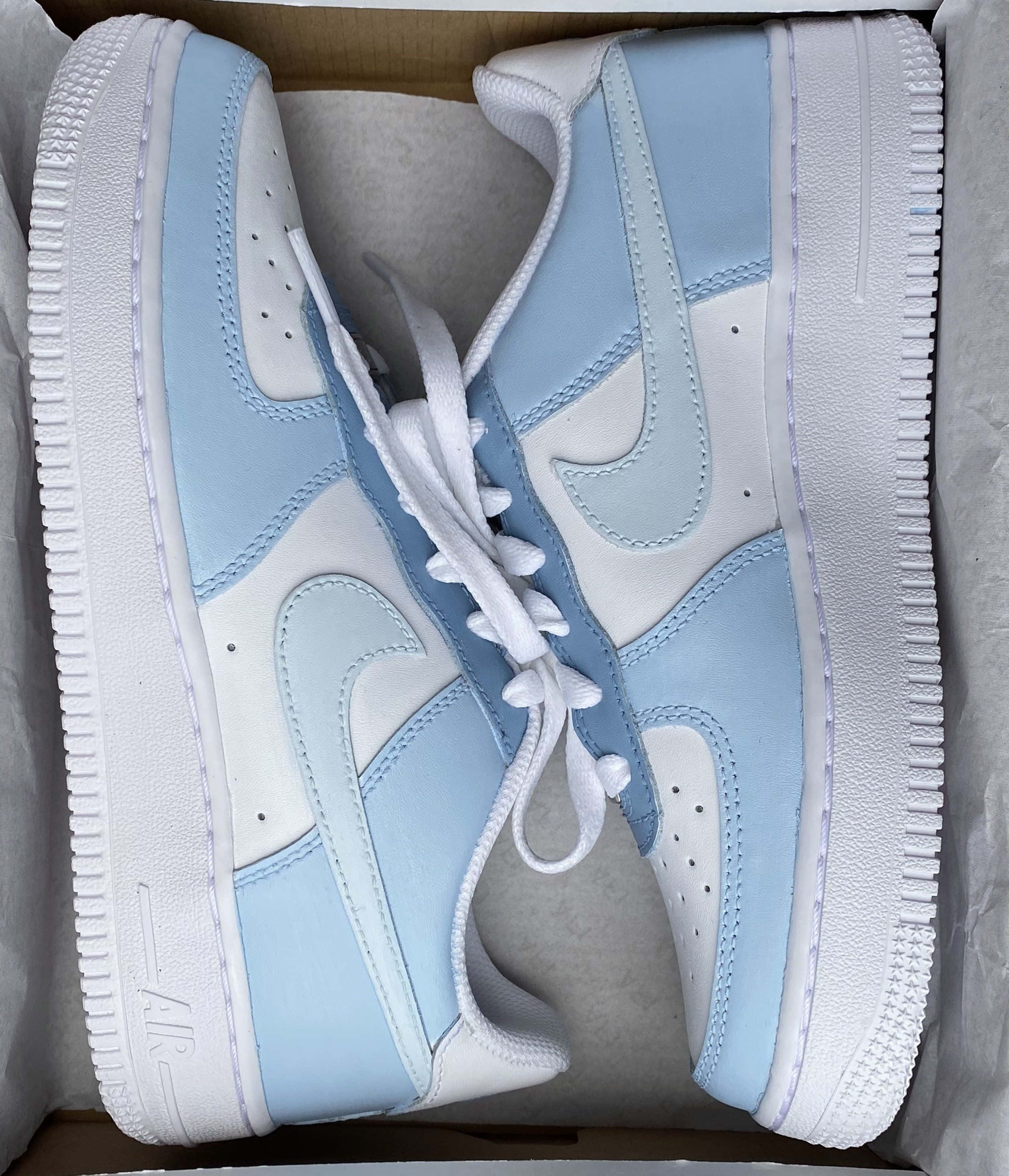 Nike Air Force 桌布 壁紙 — 一雙淺藍色和白色的Nike Air Force 1運動鞋整齊地放在紙盒內，附有紙巾。