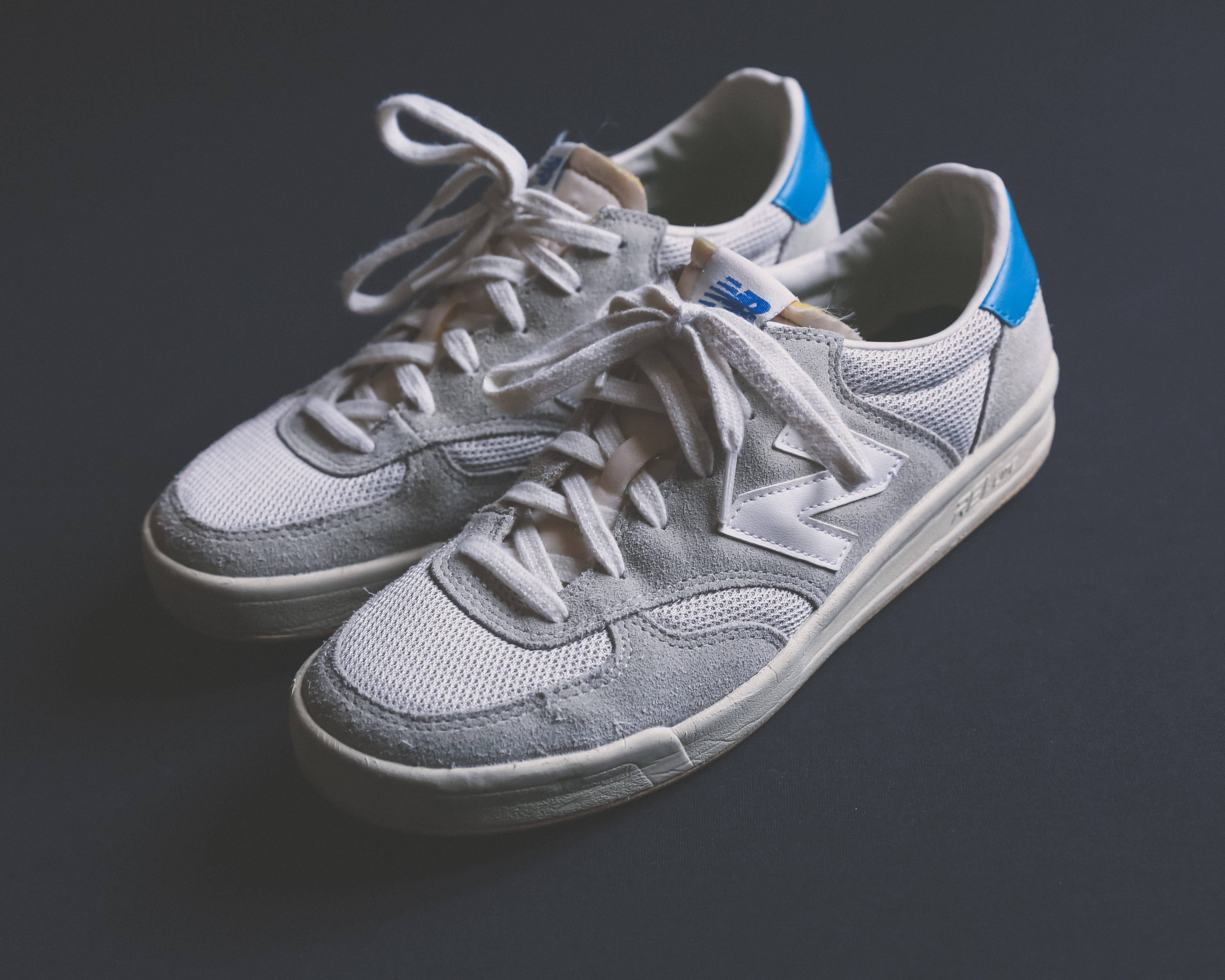 New 桌布 壁紙 — 一雙灰色 New Balance 運動鞋，帶有藍色點綴和白色鞋帶，放置在深灰色表面上。